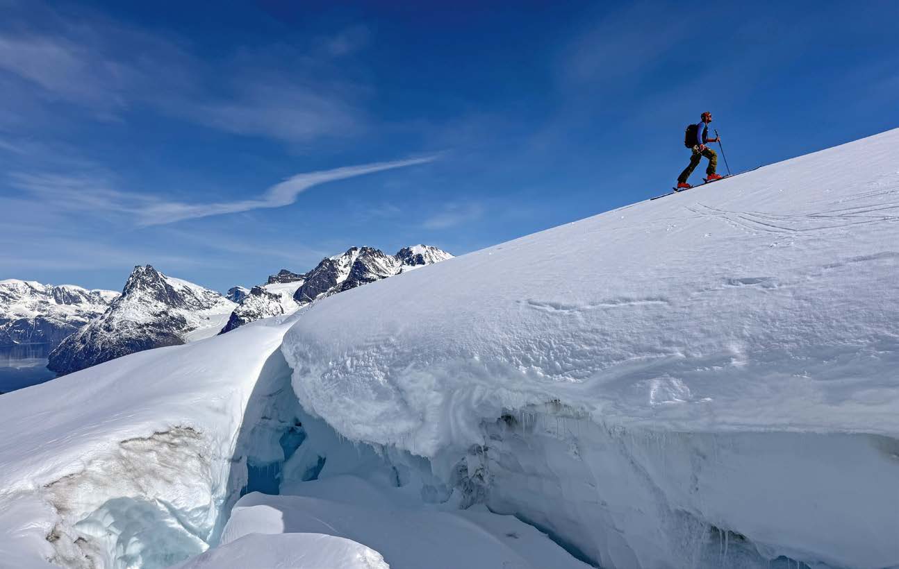 Skitourengeher steigt über eine Gletscherkante mit Blick auf Grönlands Berge