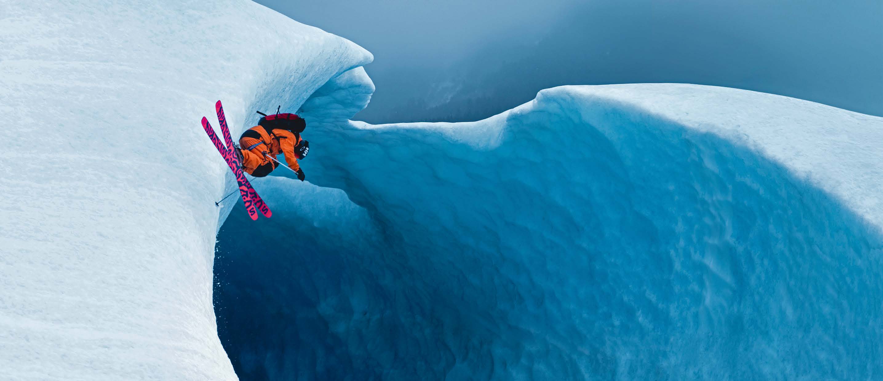 Skifahrer springt über eine geschwungene blaue Eiskante am Sheridan Glacier
