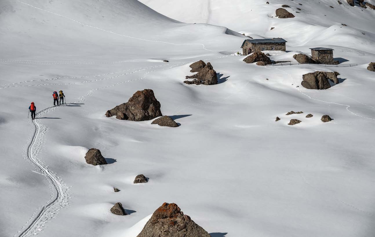 Skitourengruppe zieht ihre Spur zwischen Felsblöcken zu einer Steinhütte