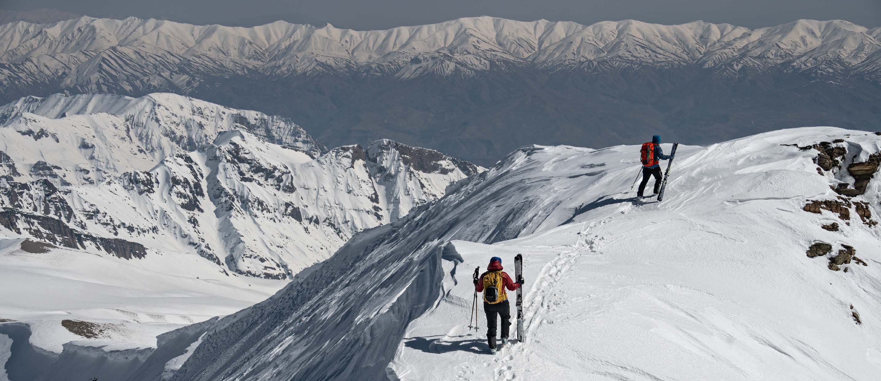 Skitourengeher auf einem verschneiten Grat über dunstigen Tälern in Iran