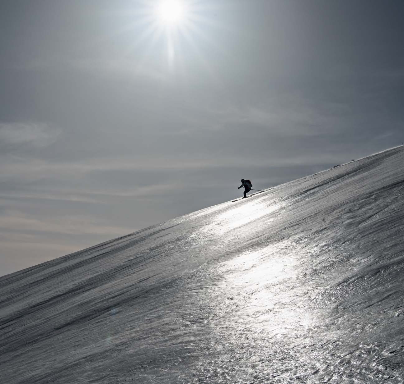 Skifahrer im Gegenlicht auf einem glitzernden vereisten Hang