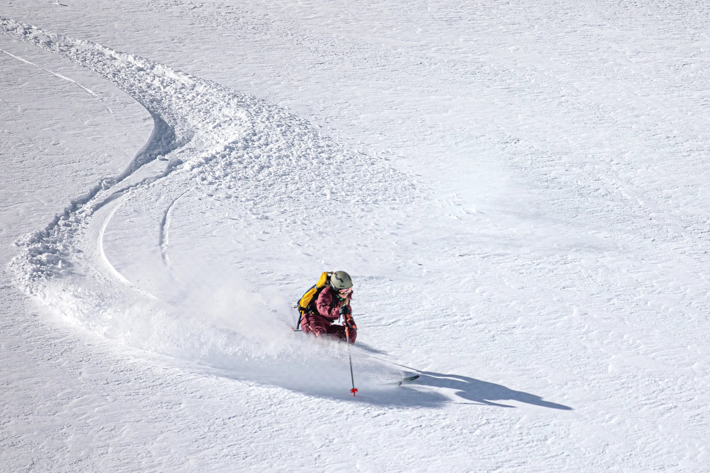 Andrea Limbacher zieht mit gelbem Rucksack einen Schwung durch den Tiefschnee in Gastein und hinterlässt eine geschwungene Spur auf dem offenen Hang.