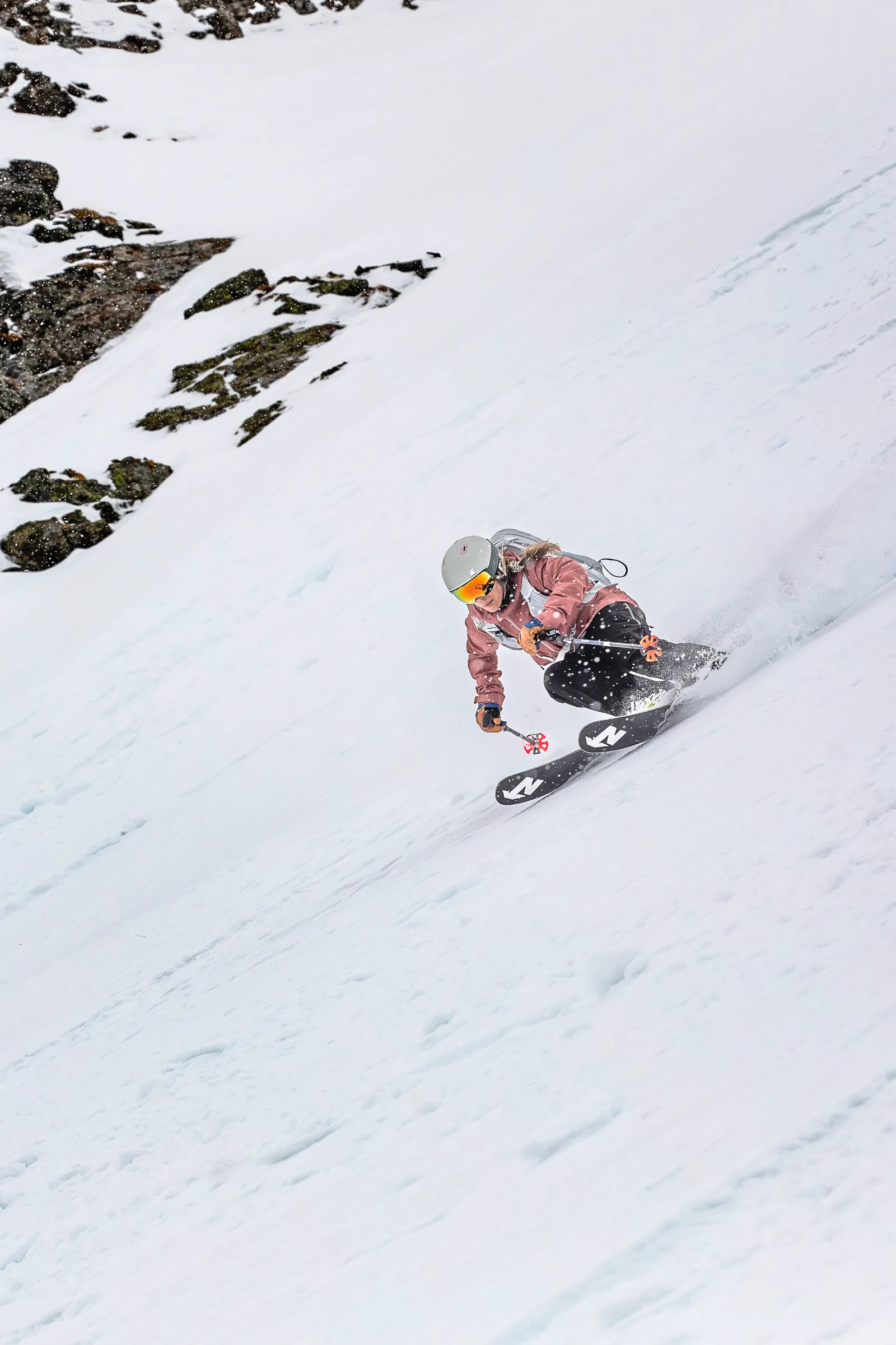 Andrea Limbacher zieht einen Freeride-Schwung durch einen verschneiten Hang unterhalb von Felsen in Lenzerheide.