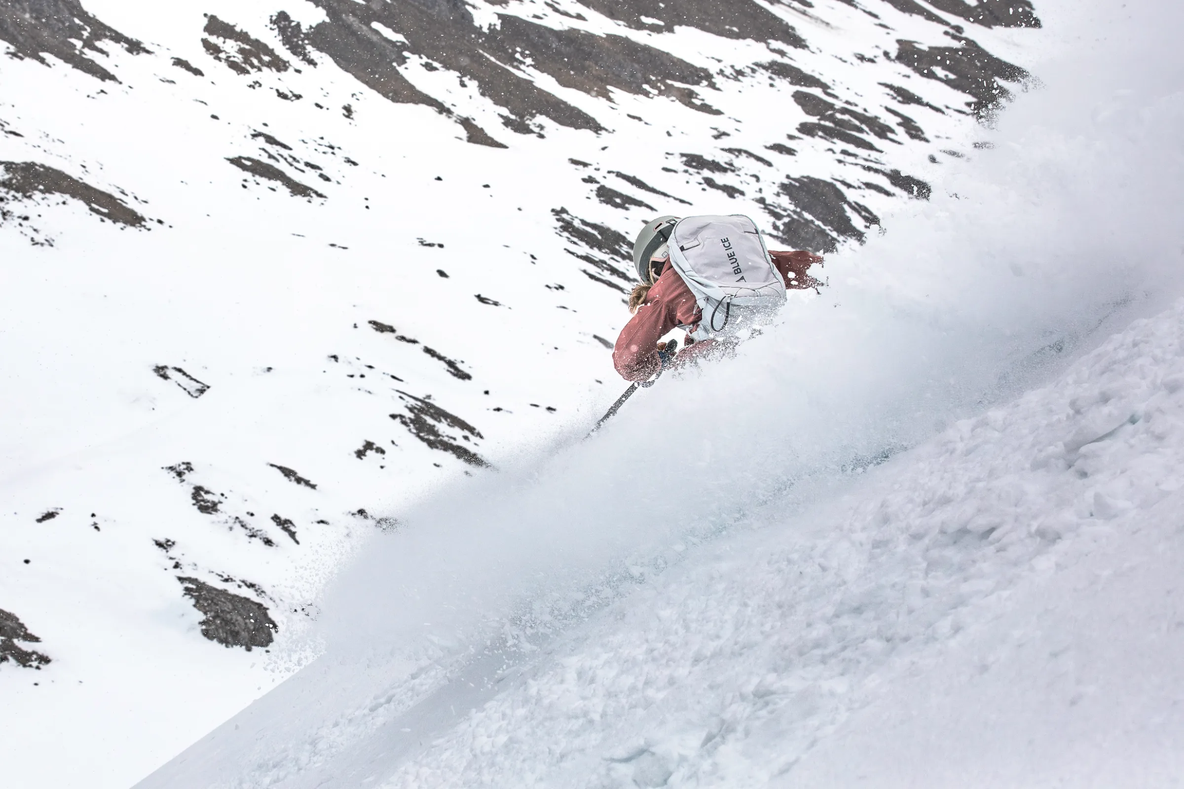 Andrea Limbacher bei einer Tiefschneeabfahrt vor schneebedeckten Felsflanken in Lenzerheide, aufgenommen von hinten.