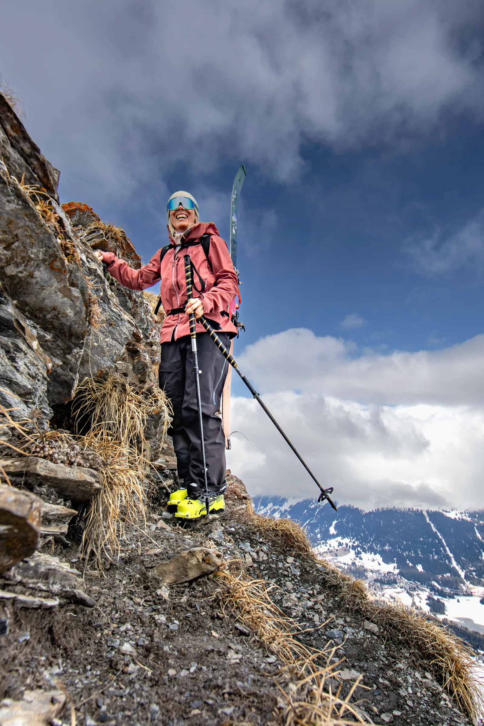 Andrea Limbacher steht mit Skischuhen und Skistöcken auf einem schmalen Felsweg oberhalb verschneiter Berge in Lenzerheide.