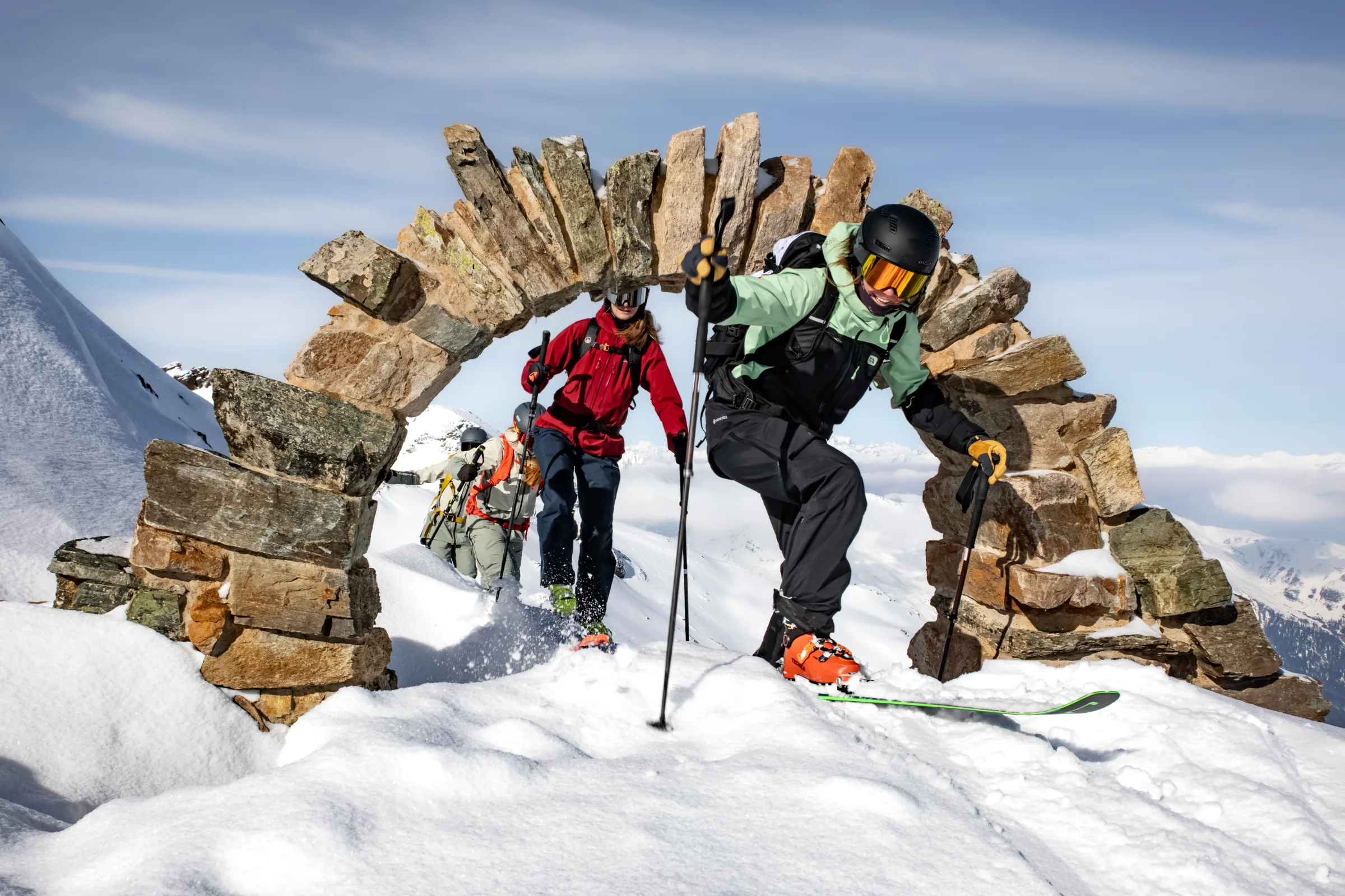 Annika Schlachter bewegt sich mit Ski und Stöcken durch einen Steinbogen im Schnee bei Lenzerheide, gefolgt von weiteren Personen mit Skiausrüstung.