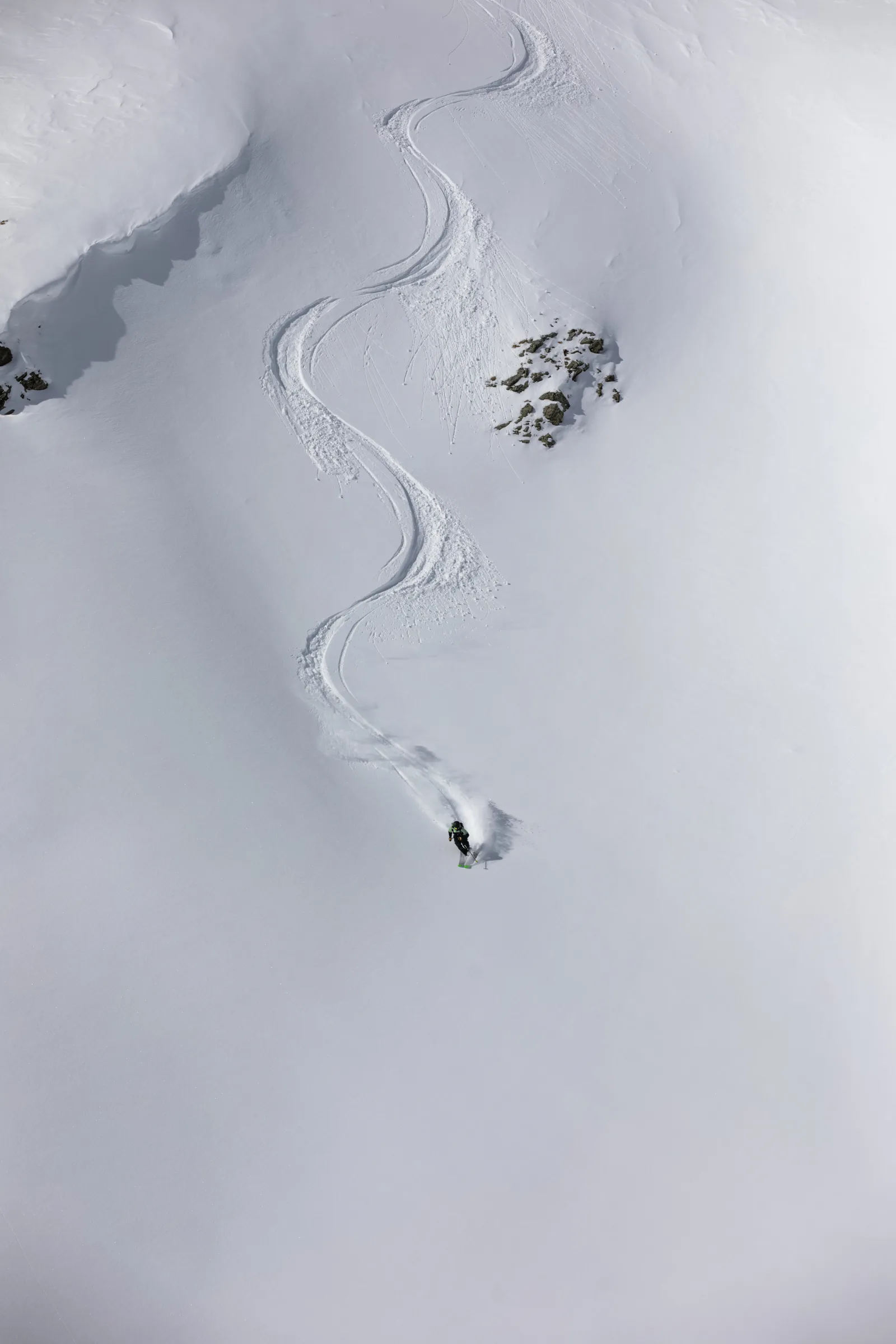 Annika Schlachter zieht einen Schwung auf einem weiten Tiefschneehang; ihre S-förmige Spur führt zwischen Felsen von weit oben herab.