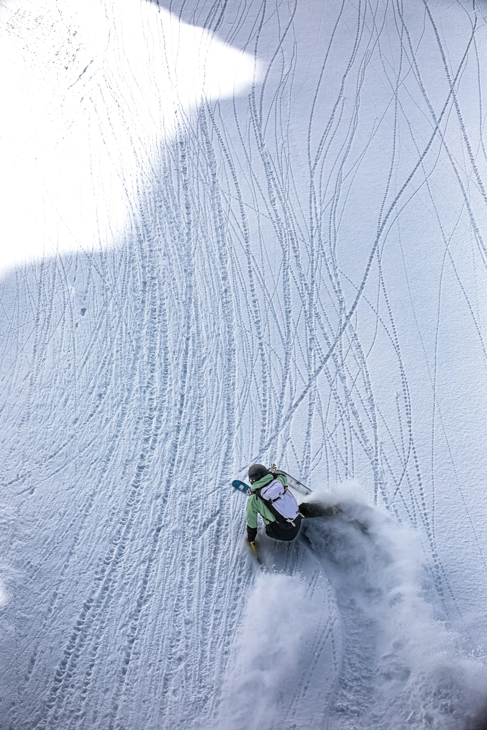 Von hinten gesehen legt sich Annika Schlachter tief in einen Skischwung und wirbelt auf einem von feinen Spuren durchzogenen Schneehang Schnee auf.