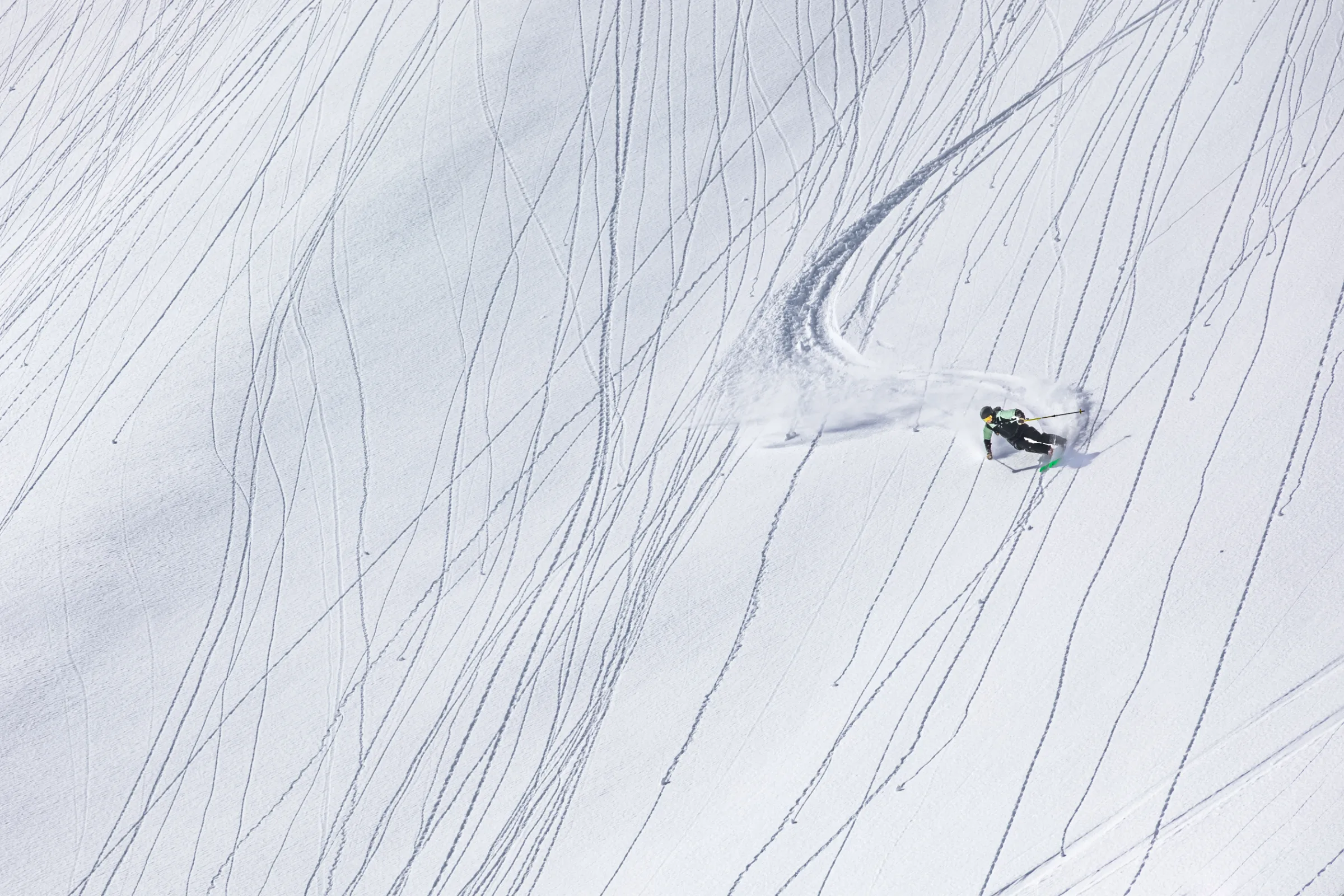 Annika Schlachter lehnt sich auf einem weiten, von feinen Spuren durchzogenen Schneehang in einen Schwung und hinterlässt eine breite Kurve mit aufsprühendem Schnee.