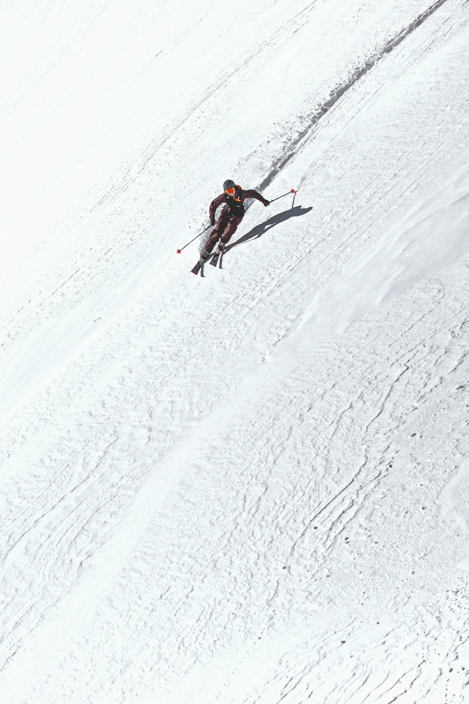 Bernd Hassmann fährt mit seitlich gehaltenen Skistöcken einen weiten Schneehang hinab; hinter ihm verlaufen seine Spur und ein markanter Schatten.