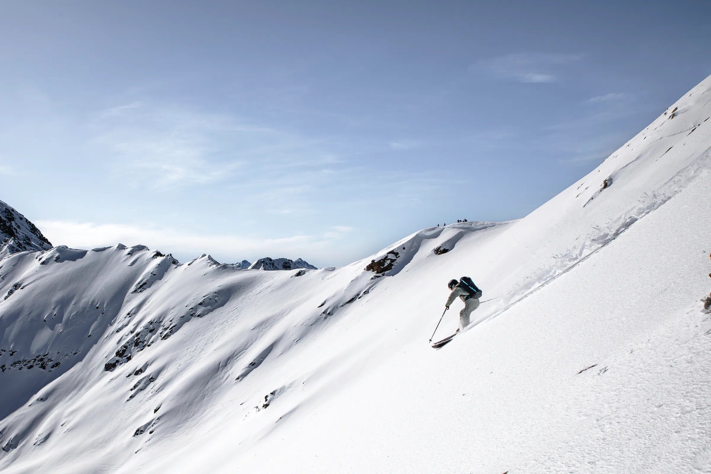 Bernd Hassmann fährt mit Rucksack einen steilen, offenen Schneehang bei Lenzerheide hinab, umgeben von felsigen, verschneiten Graten.