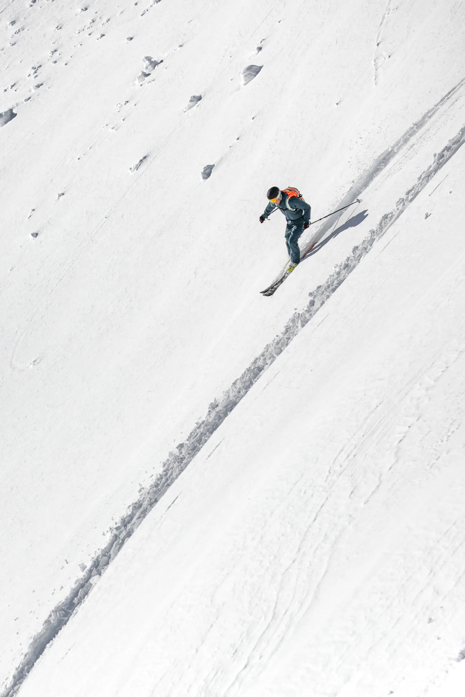 Christoph Öfele fährt mit orangefarbenem Rucksack einen steilen Schneehang in Gastein hinab, neben einer langen diagonalen Skispur.