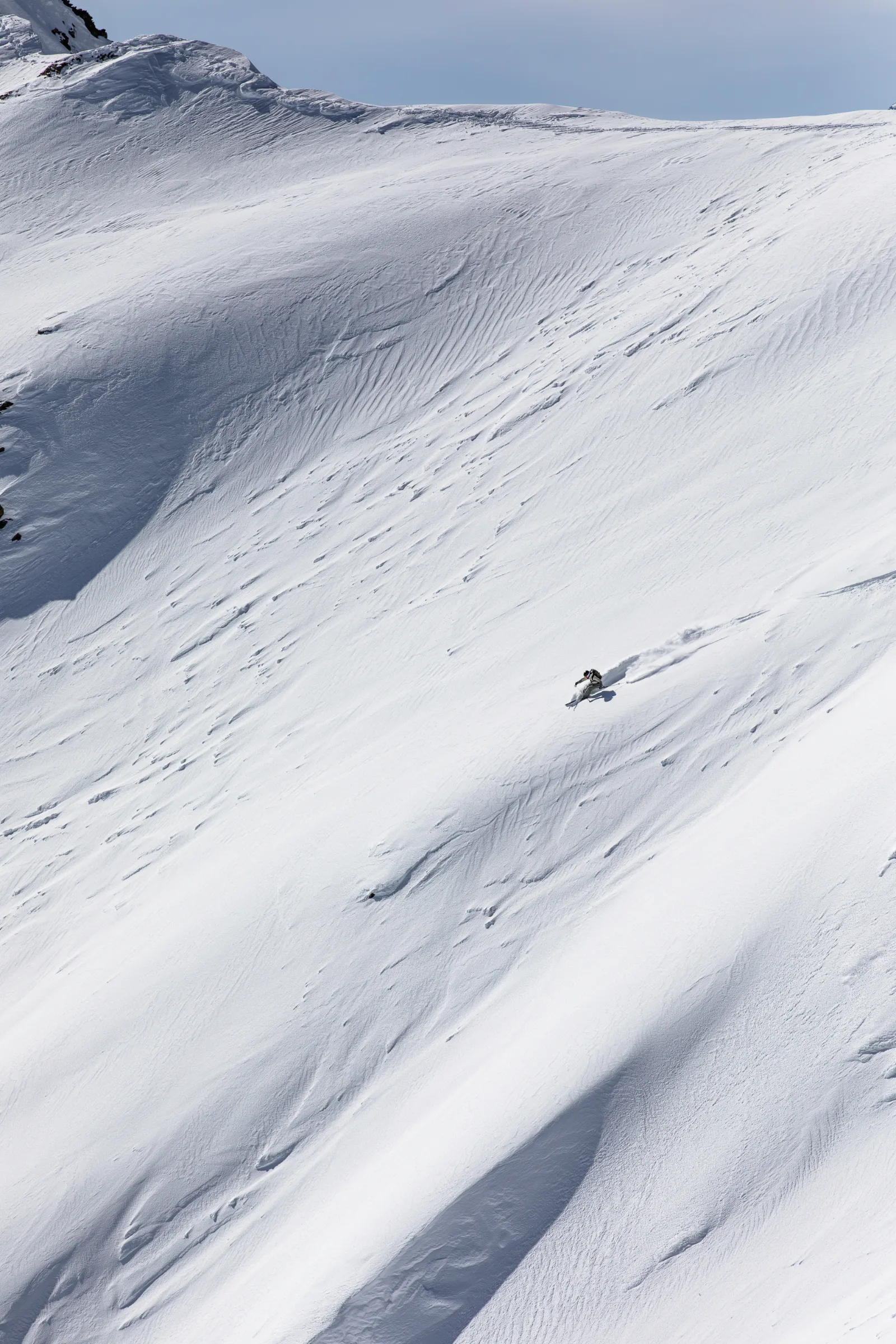 Claudia Kohler zieht einen Schwung über einen weiten, von Schneerippen gezeichneten Hang in Lenzerheide und hinterlässt eine Schneefahne.