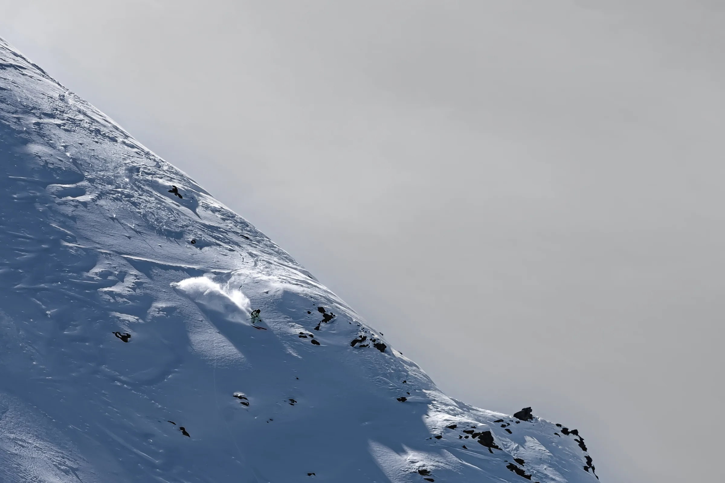 Claudia Kohler zieht auf einem steilen, felsdurchsetzten Schneehang in Lenzerheide einen Schwung und wirbelt eine helle Schneefahne auf.