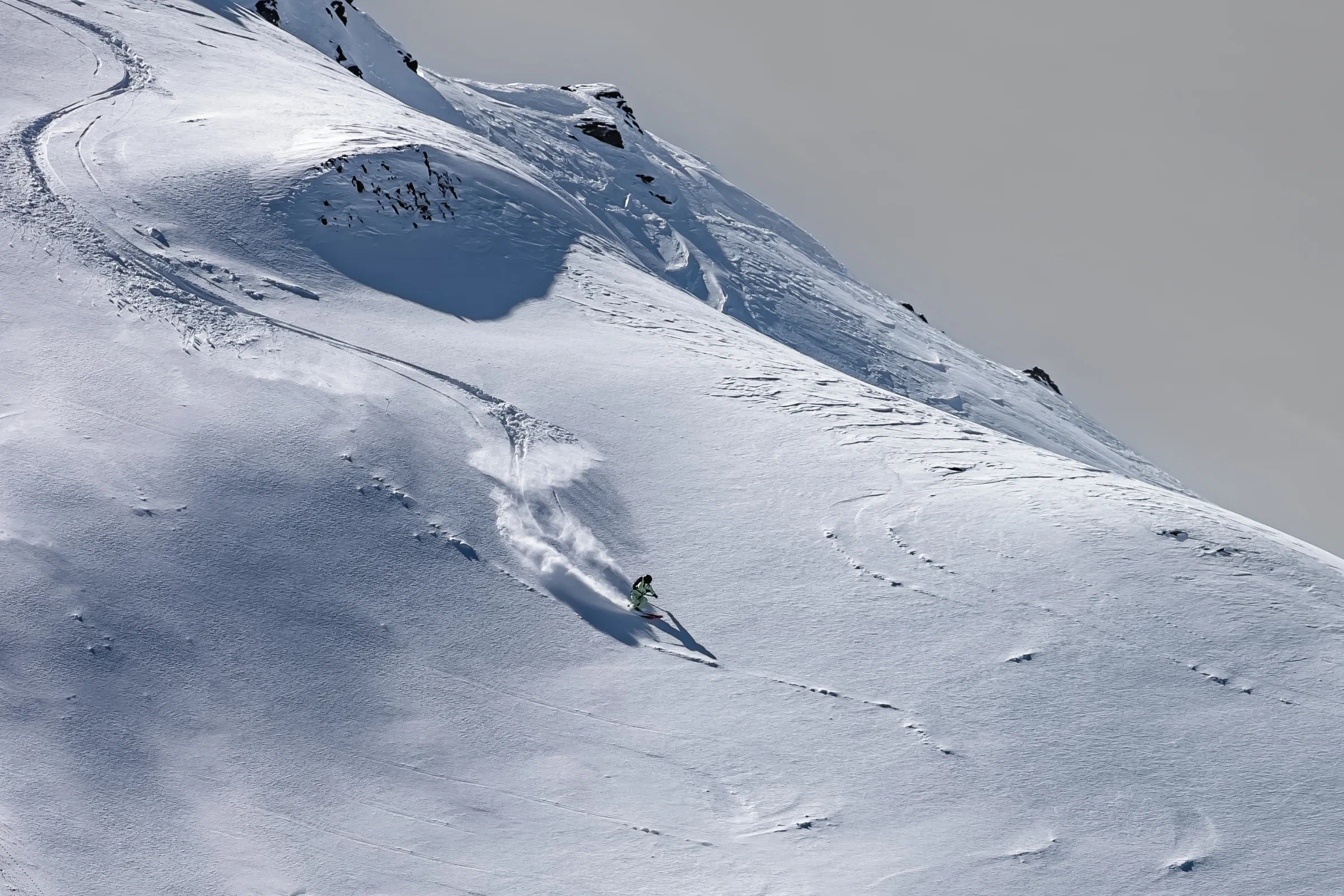 Claudia Kohler fährt unterhalb verschneiter Felsformationen über einen weiten Hang und hinterlässt eine geschwungene Spur im Schnee.