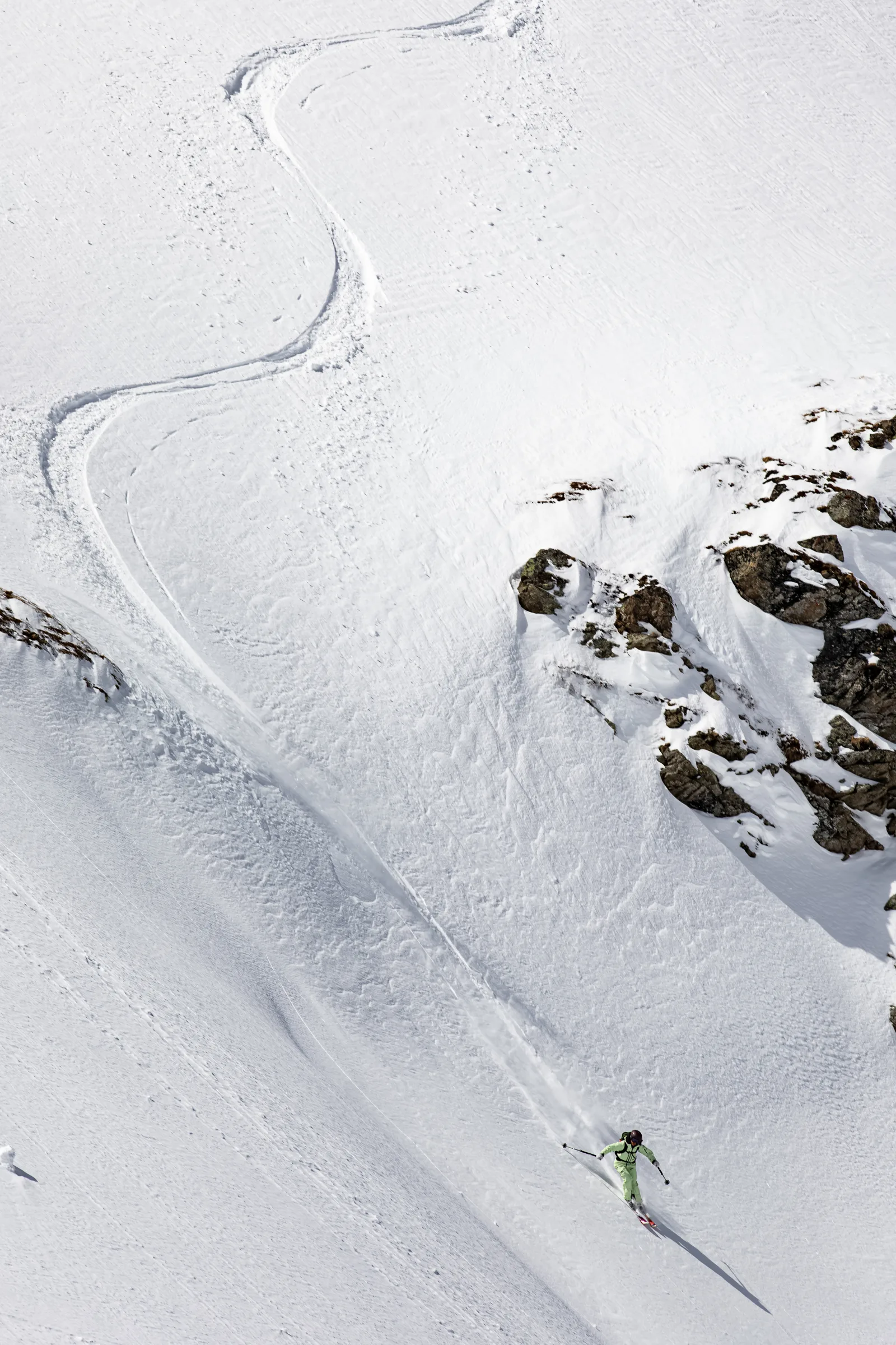 Claudia Kohler fährt in hellgrüner Kleidung einen steilen Schneehang in Lenzerheide hinab, mit geschwungenen Skispuren hinter sich und schneebedeckten Felsen rechts.