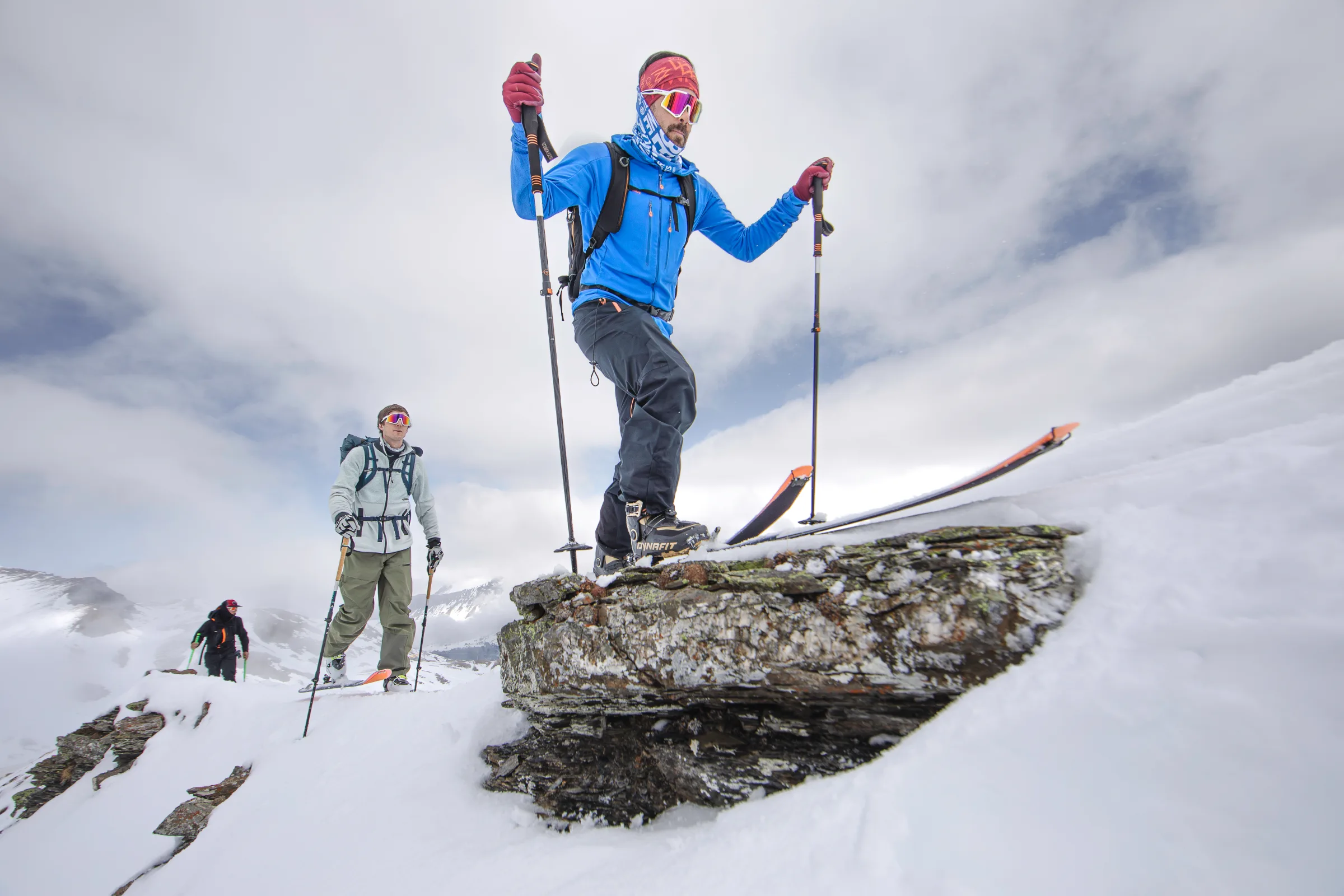 Florian Eigler steigt in blauer Jacke mit Tourenski über eine verschneite Felsstufe bei Lenzerheide, während zwei weitere Personen folgen.
