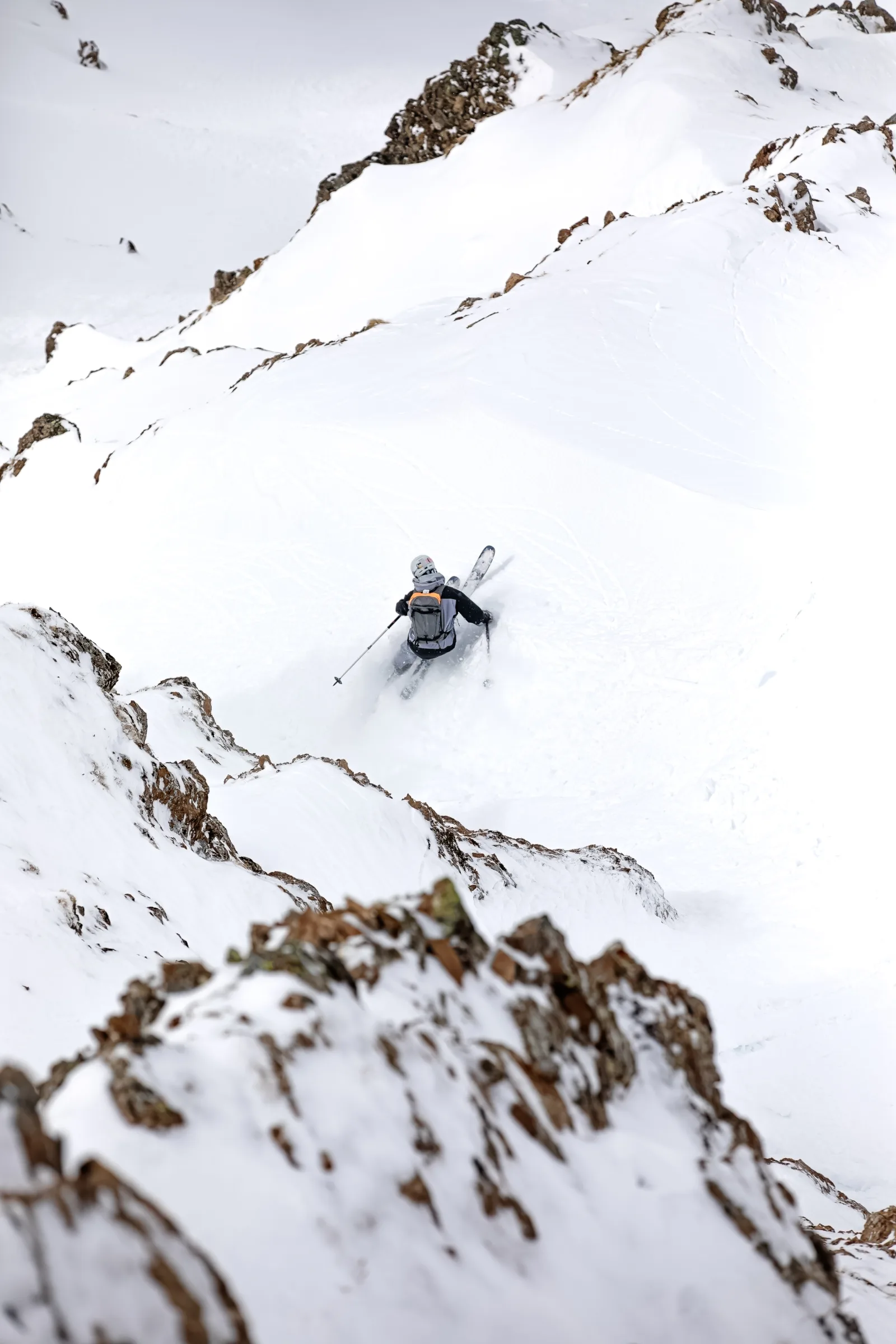 Florian Eigler fährt mit Helm und Rucksack durch tiefen Schnee zwischen schroffen Felsen in Lenzerheide, von hinten gesehen.