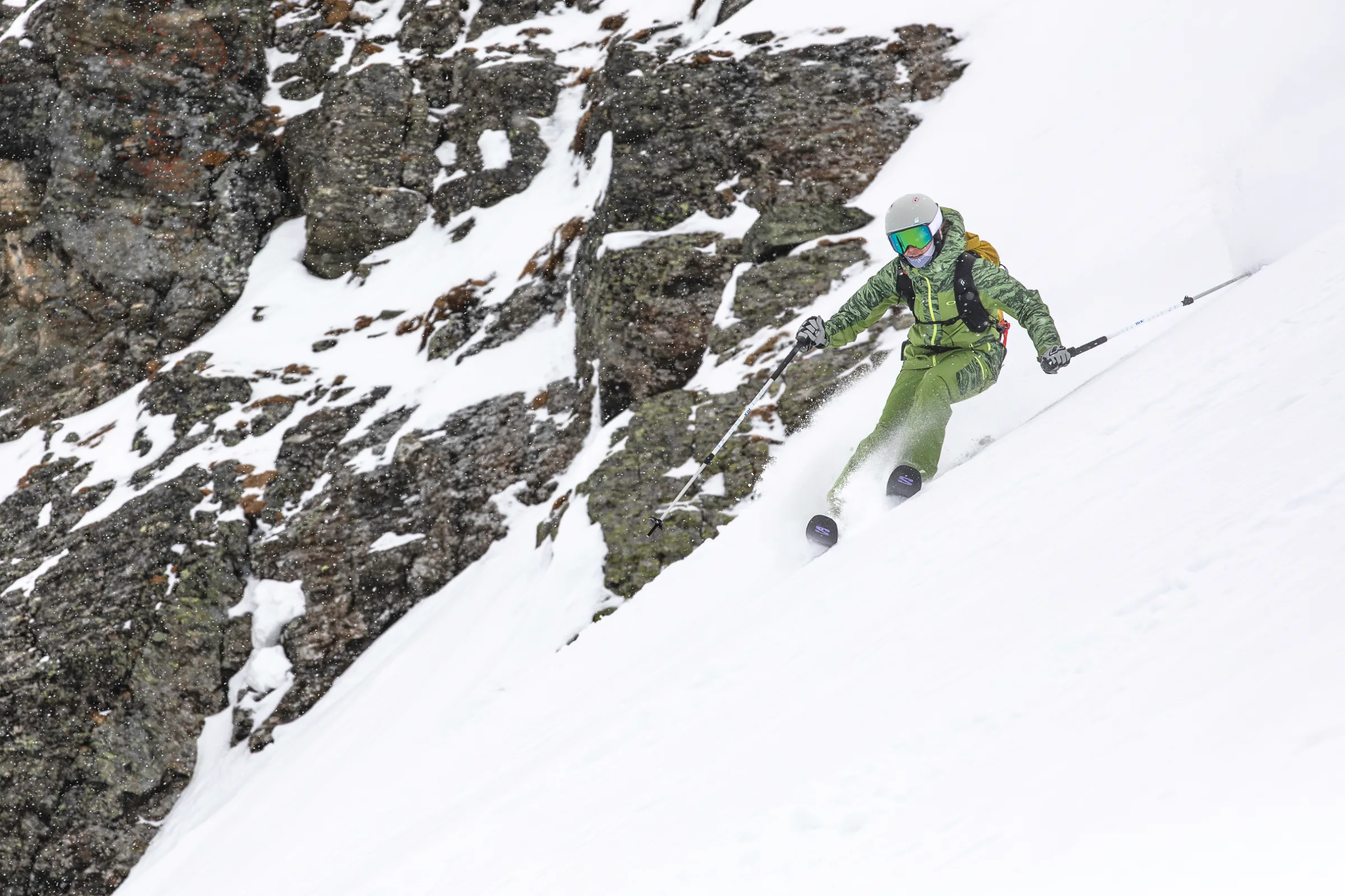 Martina Wengenmeir fährt mit weit auseinander gehaltenen Skistöcken vor einer schneebedeckten Felswand bergab.