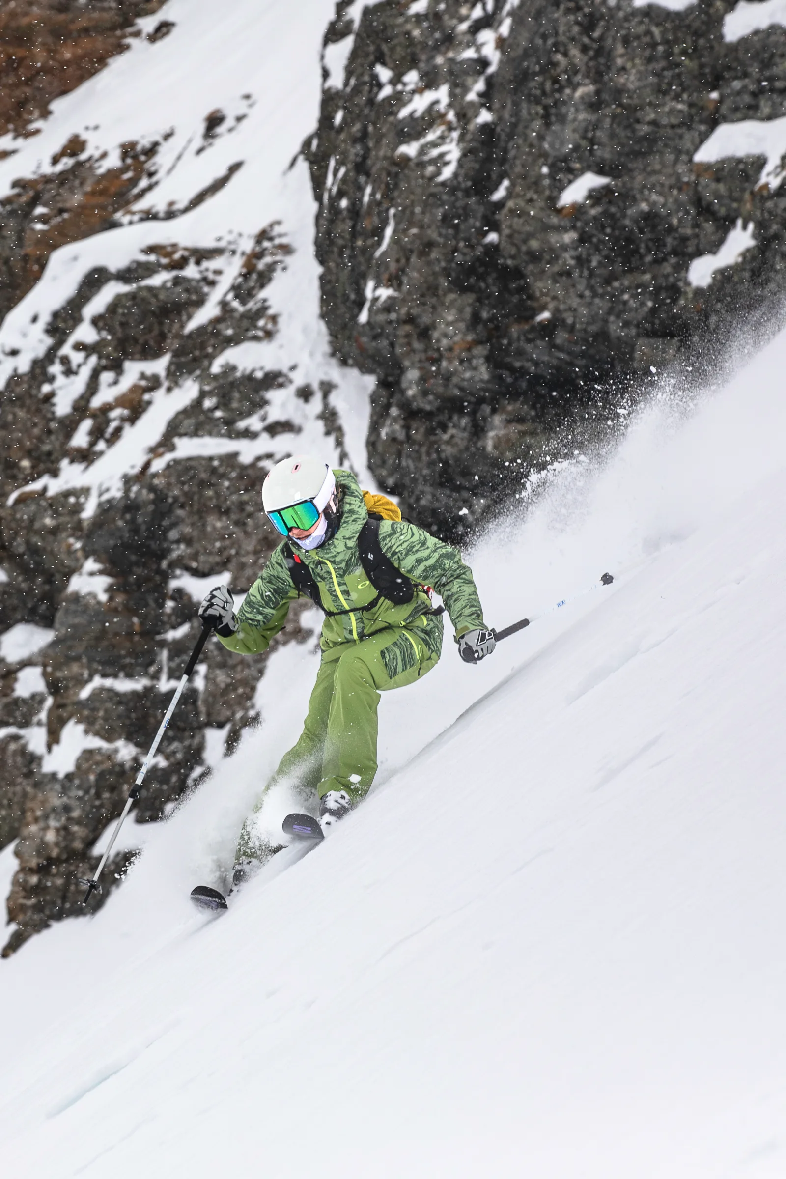 Martina Wengenmeir zieht vor dunklen Felsen einen Schwung durch den Schnee, während eine hohe Schneefahne hinter ihr aufsteigt.