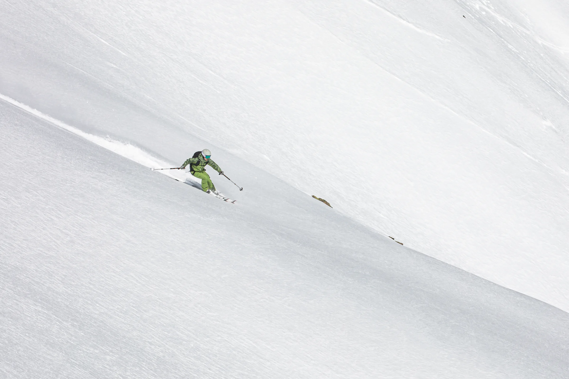 Martina Wengenmeir fährt in grüner Skikleidung diagonal über einen weiten Schneehang in Lenzerheide und zieht eine schmale Spur hinter sich.