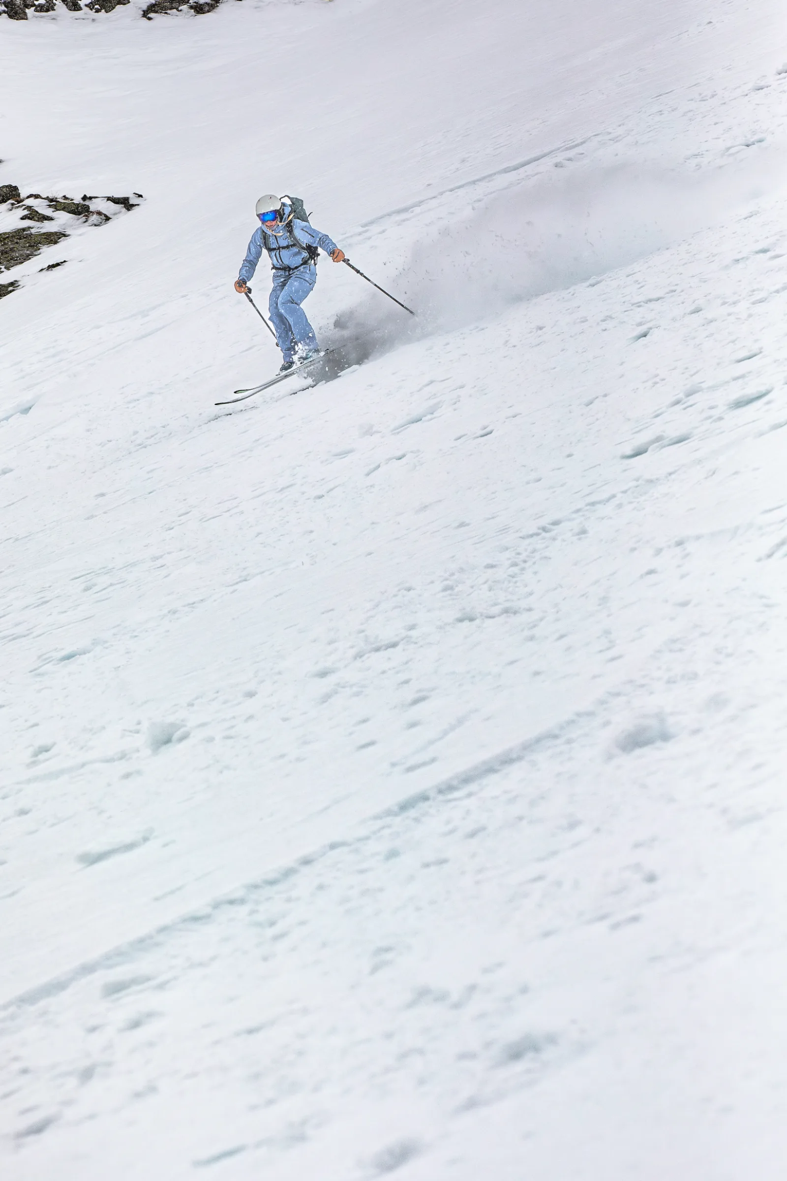 Michaela Casotti fährt mit seitlich gehaltenen Stöcken einen weiten Schneehang hinab und zieht eine Schneewolke hinter sich her.
