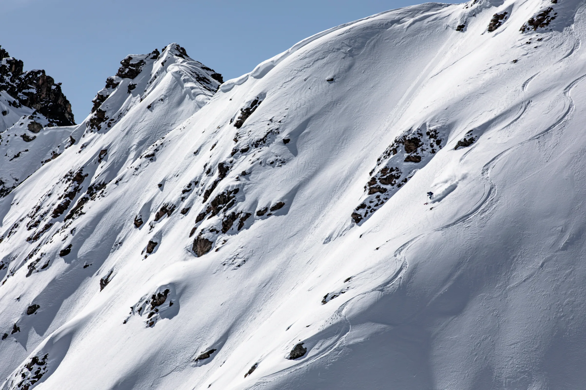 Michaela Casotti fährt durch Pulverschnee einen steilen, felsdurchsetzten Hang in Lenzerheide hinab, neben geschwungenen Skispuren.