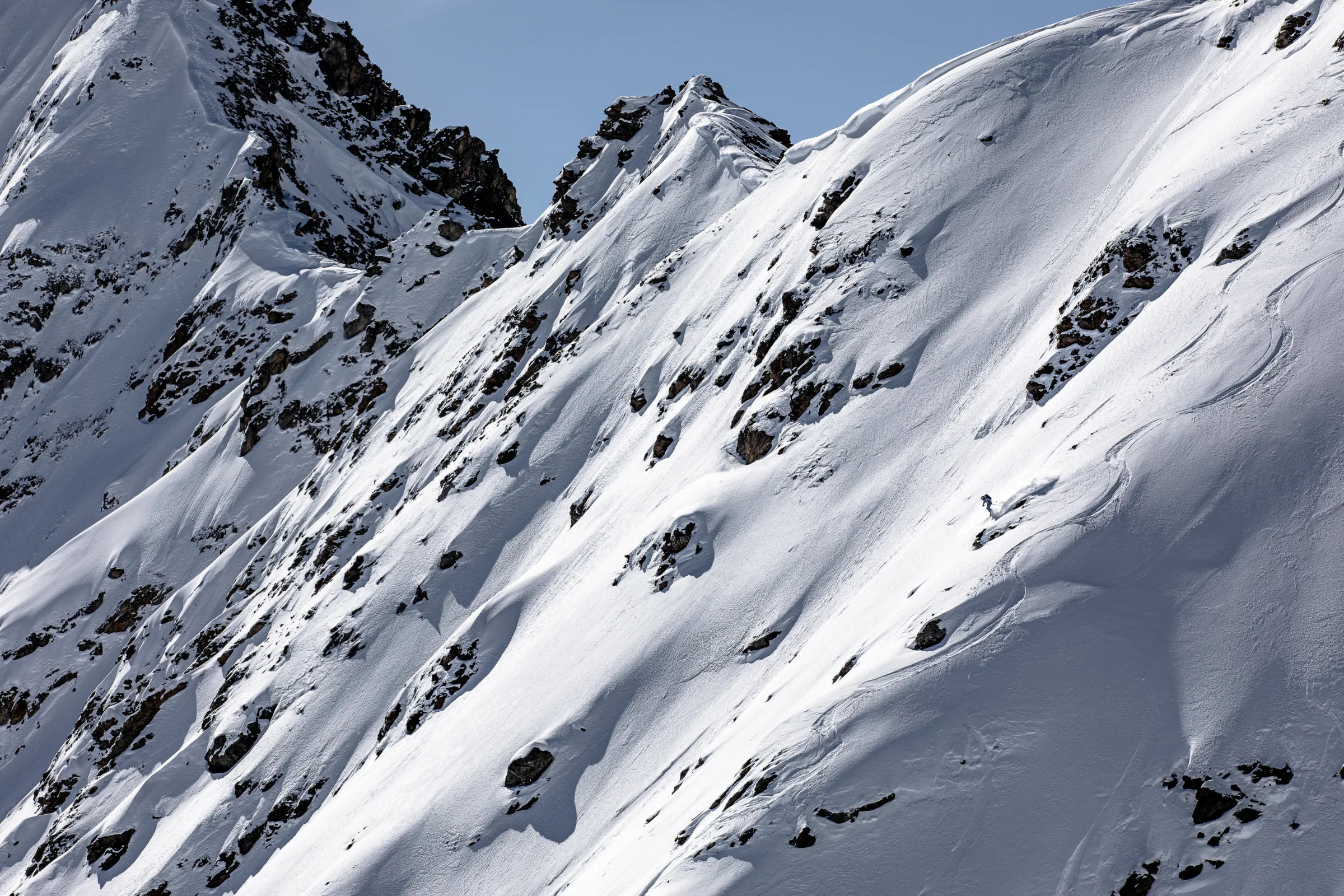 Michaela Casotti fährt zwischen freiliegenden Felsen einen weiten Schneehang hinab, über dem gezackte Grate aufragen.