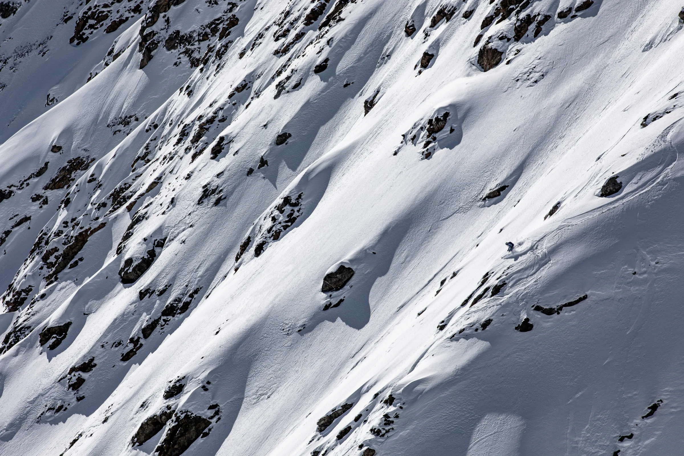 Michaela Casotti beugt sich bei der Abfahrt über einen steilen, felsdurchsetzten Schneehang nach vorn und wirbelt Schnee auf.