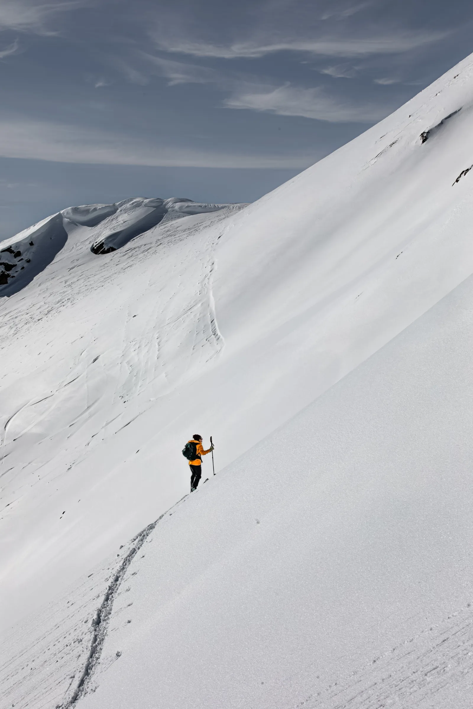 Michaela Casotti folgt mit Tourenski und Stöcken einer schmalen Aufstiegsspur quer über einen steilen, offenen Schneehang.