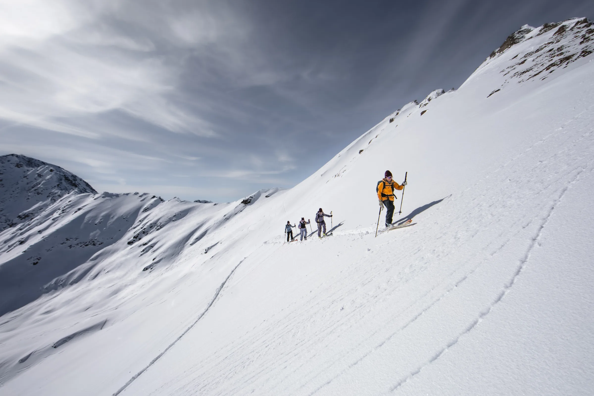 Michaela Casotti steigt in orangefarbener Jacke vor drei weiteren Skitourengehenden über einen steilen Schneehang bei Lenzerheide auf.
