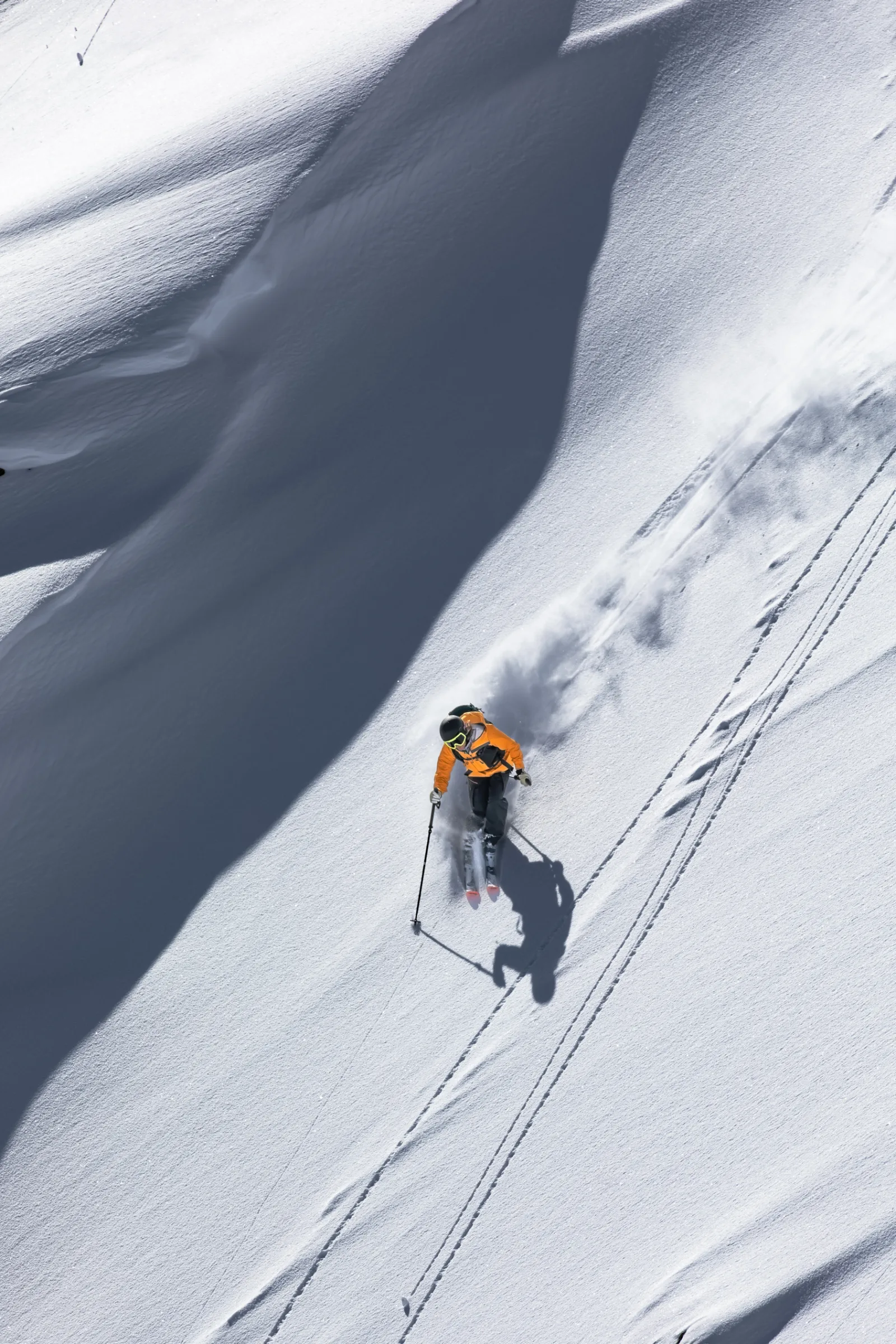 Michaela Casotti fährt in orangefarbener Jacke einen steilen Schneehang in Lenzerheide hinab, zieht eine Schneefahne hinter sich her und wirft einen langen Schatten.