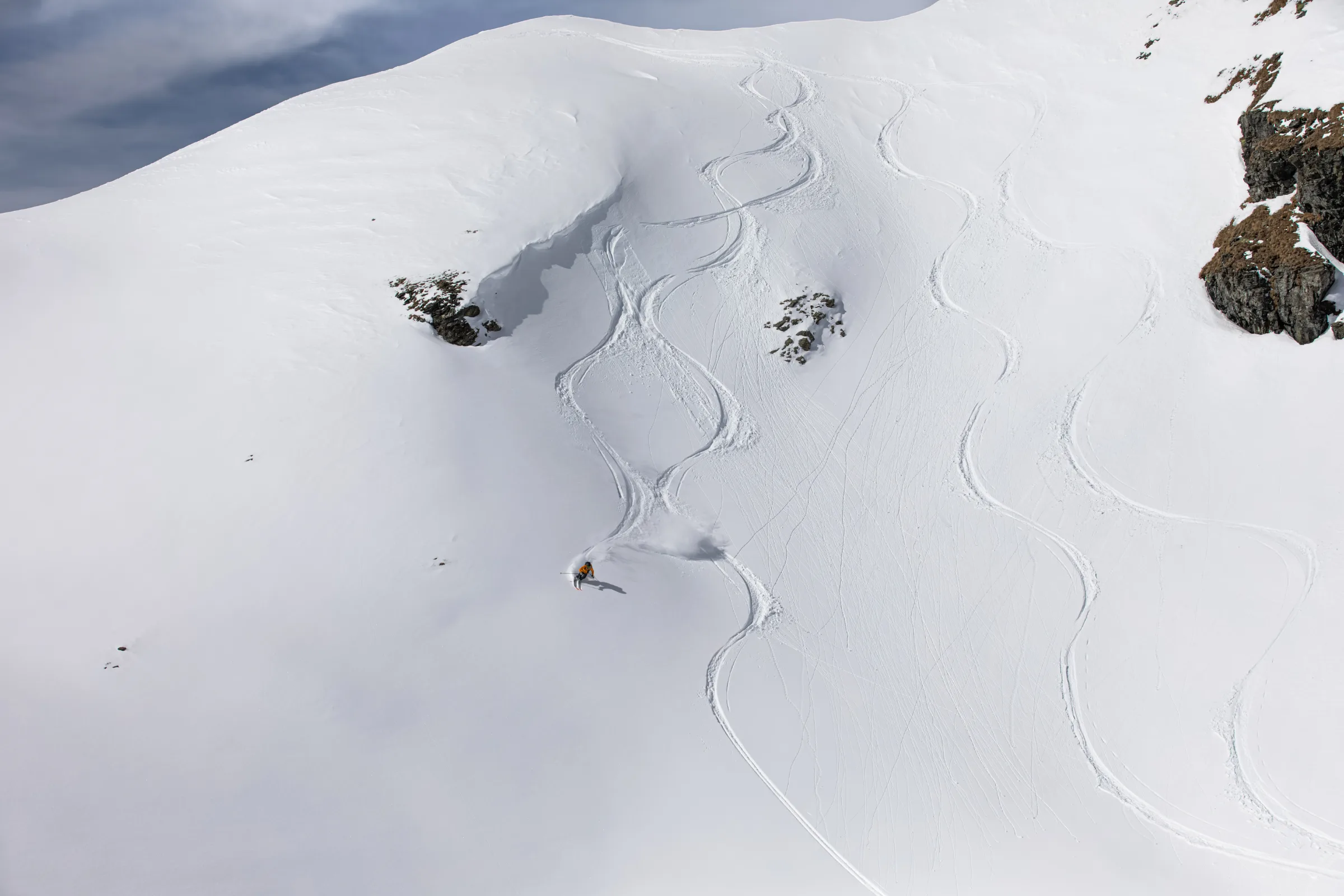 Michaela Casotti zieht einen Schwung durch den Schnee auf einem weiten Hang in Lenzerheide, unterhalb von Felsen und zahlreichen geschwungenen Skispuren.