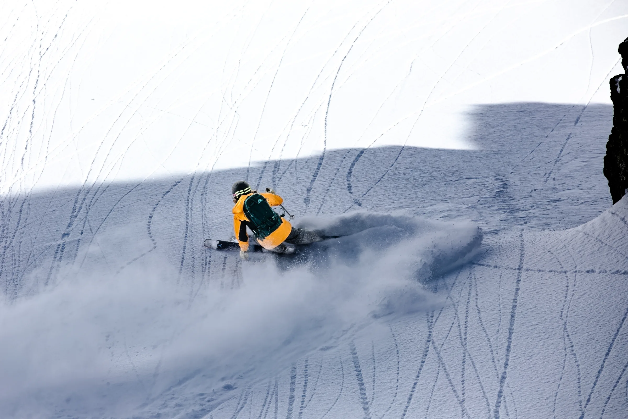 Michaela Casotti legt sich auf einem schattigen Schneehang neben einem Felsen tief in einen Skischwung und zieht eine breite Schneewolke hinter sich her.