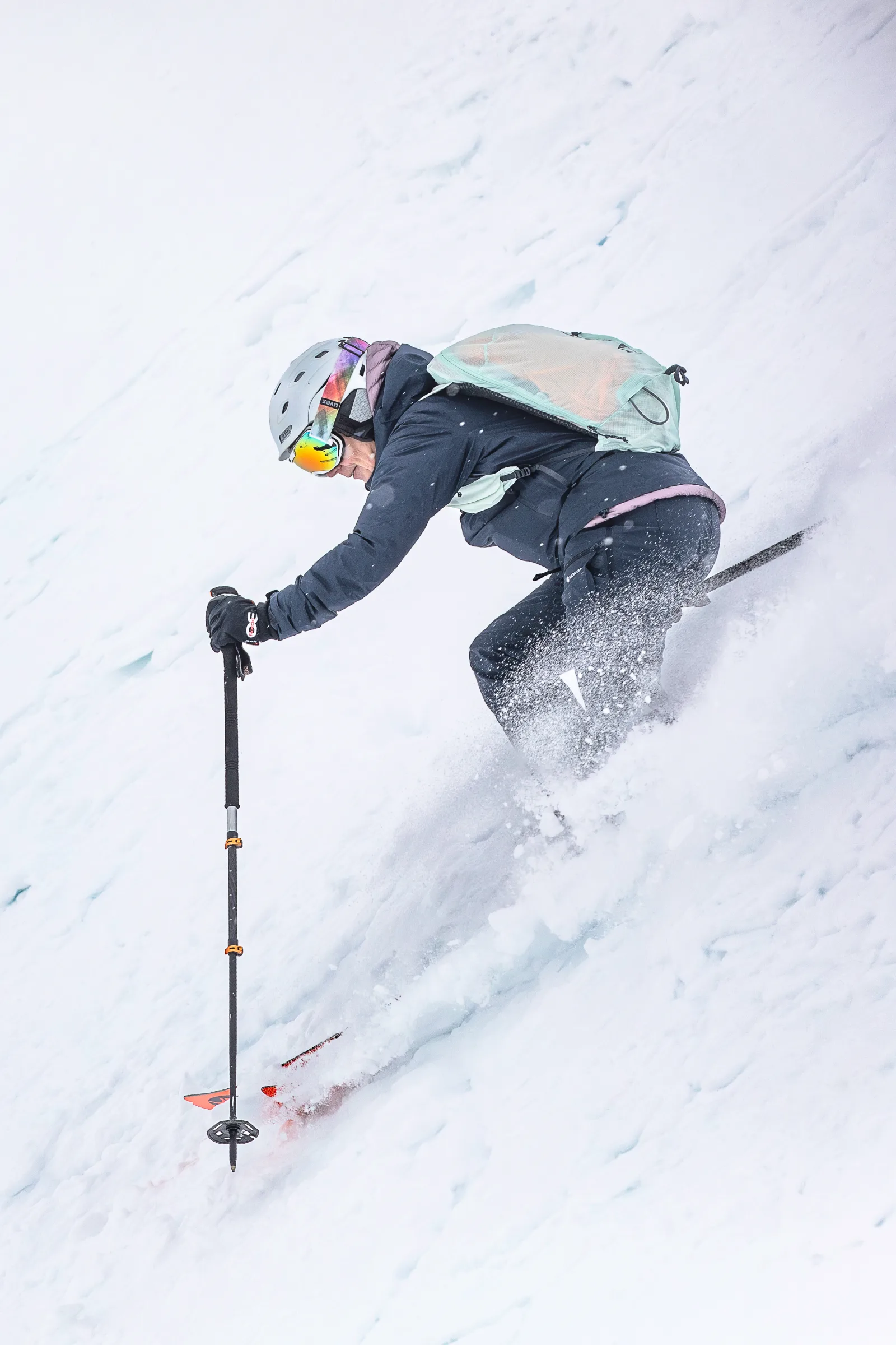 Petra Rapp beugt sich beim Skifahren tief nach vorn und führt einen Stock zum Schnee, während an ihren Beinen Schnee aufwirbelt.
