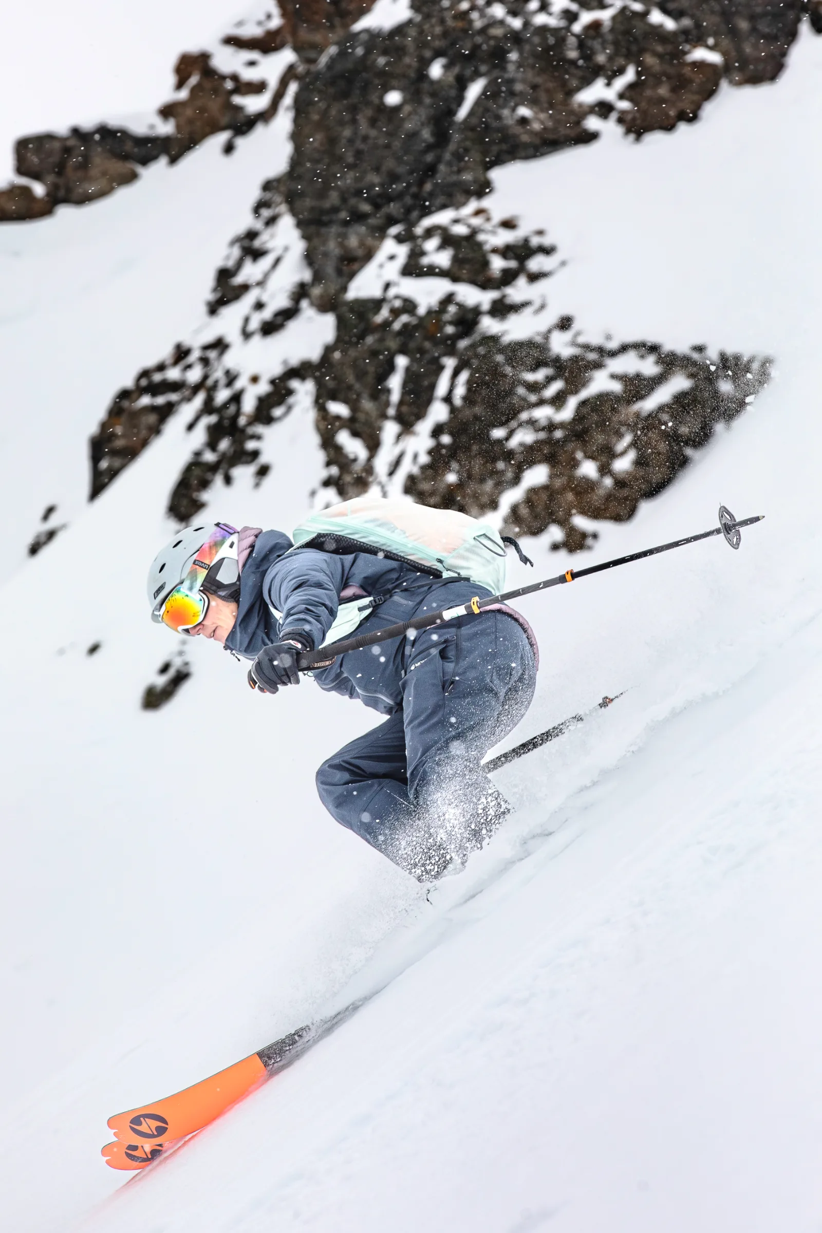 Petra Rapp fährt in tief gebeugter Haltung durch den Schnee unterhalb schneebedeckter Felsen, die Skistöcke nach hinten gerichtet.