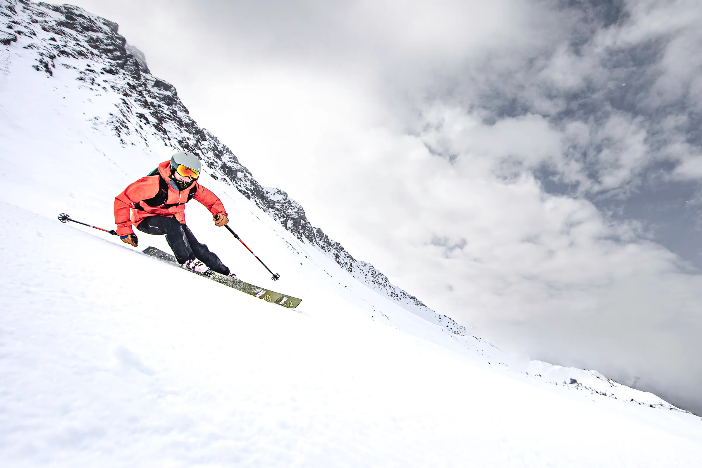 Pia Vogt fährt in roter Jacke mit gebeugten Knien über einen steilen Schneehang in Lenzerheide, hinter ihr ein felsiger Grat und Wolken.