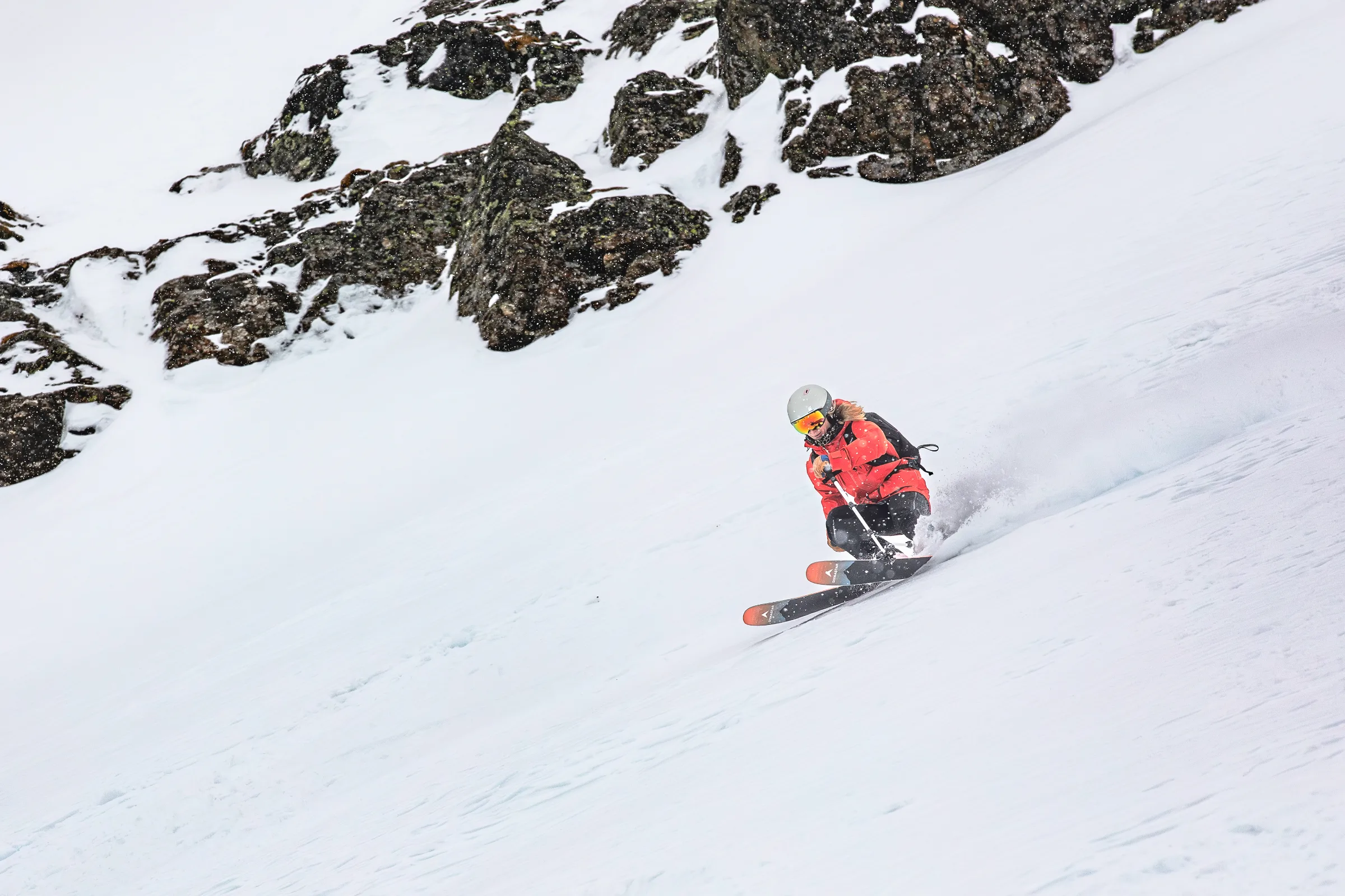 Pia Vogt zieht in tiefer Hocke einen Schwung unterhalb schneebedeckter Felsen, während hinter ihren Ski Schnee aufspritzt.