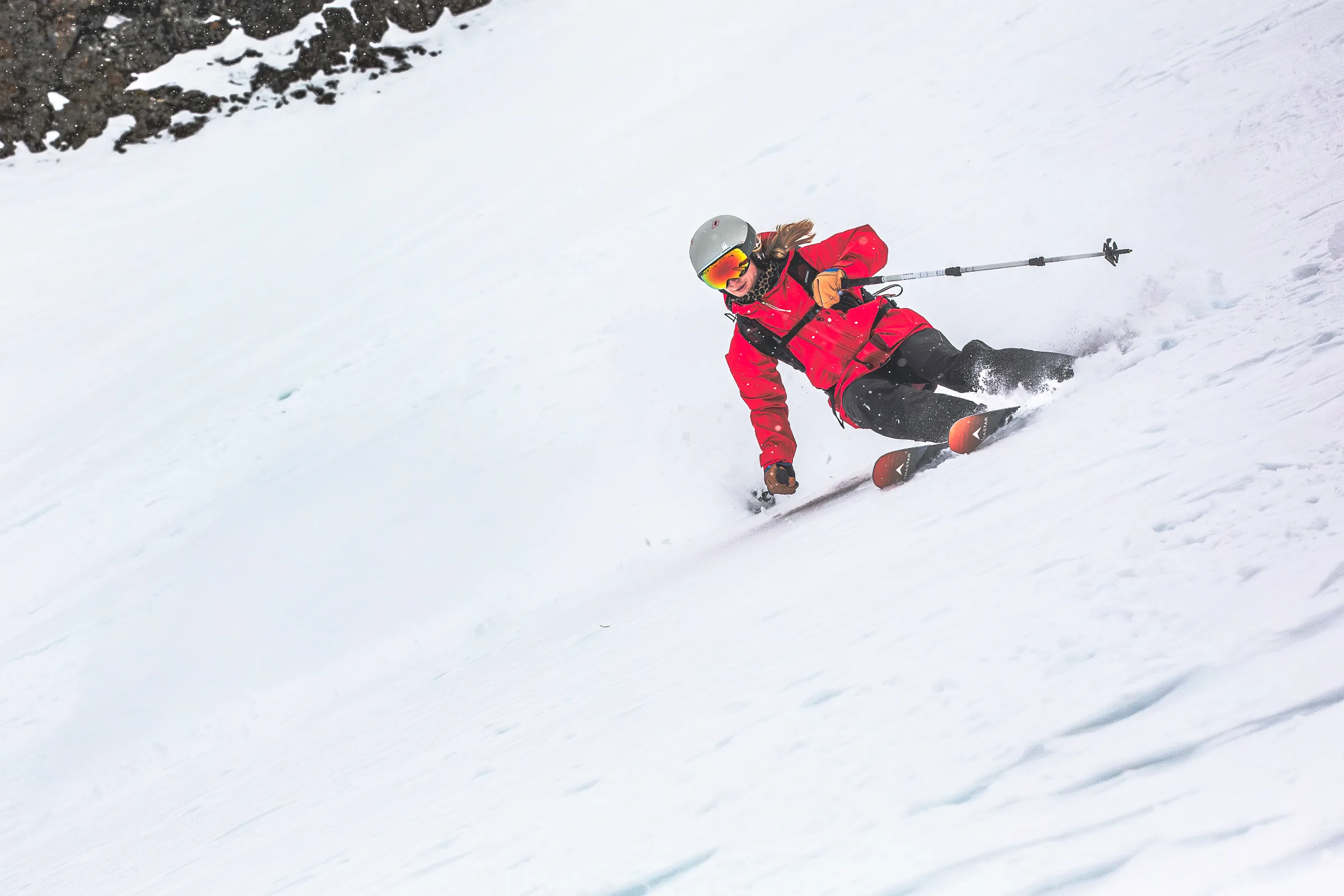 Pia Vogt lehnt sich auf einem steilen Schneehang tief in einen Schwung, eine Hand dicht über dem Schnee und einen Skistock seitlich ausgestreckt.