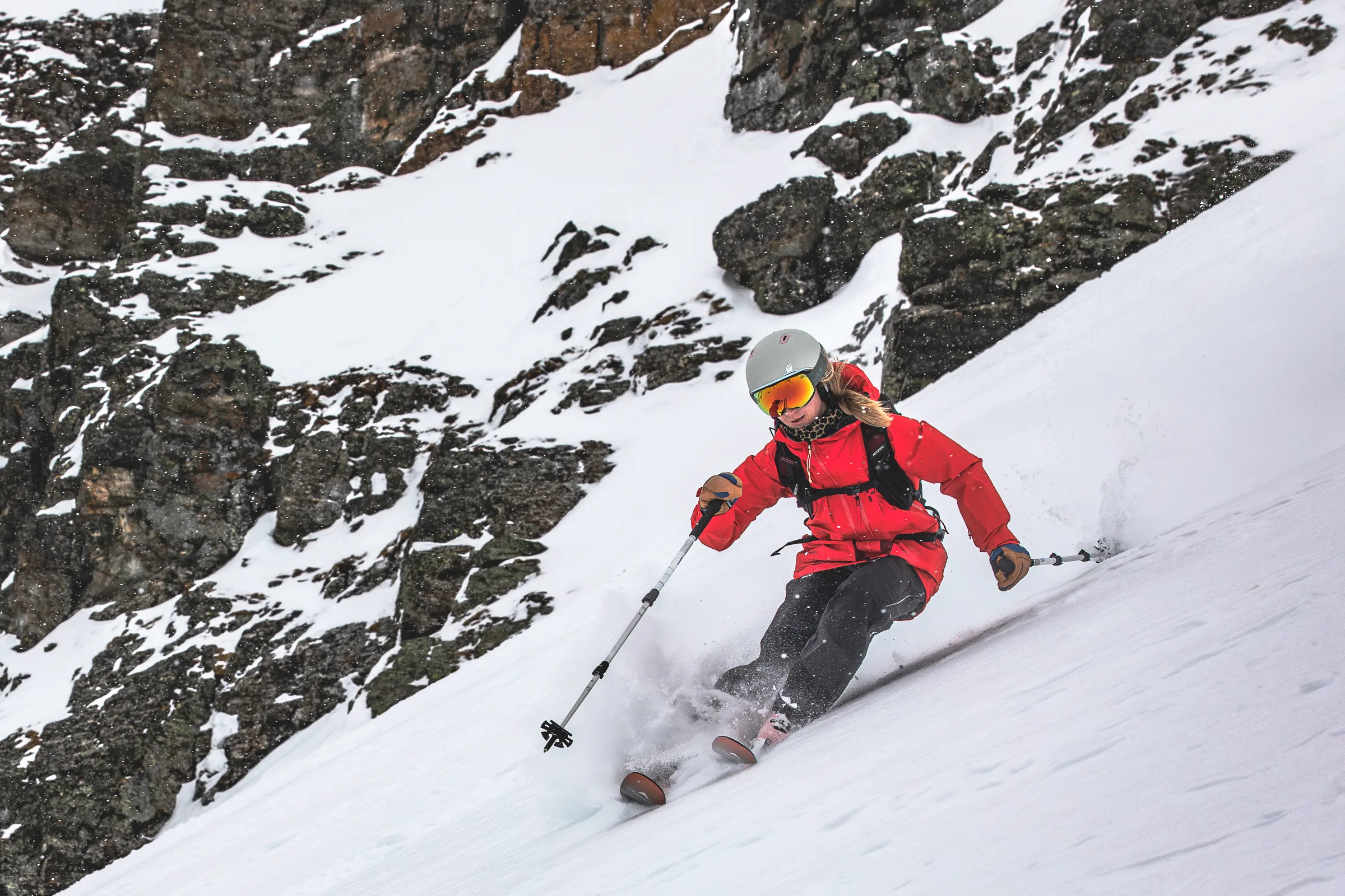 Pia Vogt fährt mit parallelen Ski und seitlich gehaltenen Stöcken an einer schneebedeckten Felswand vorbei, Schnee spritzt um ihre Schuhe.