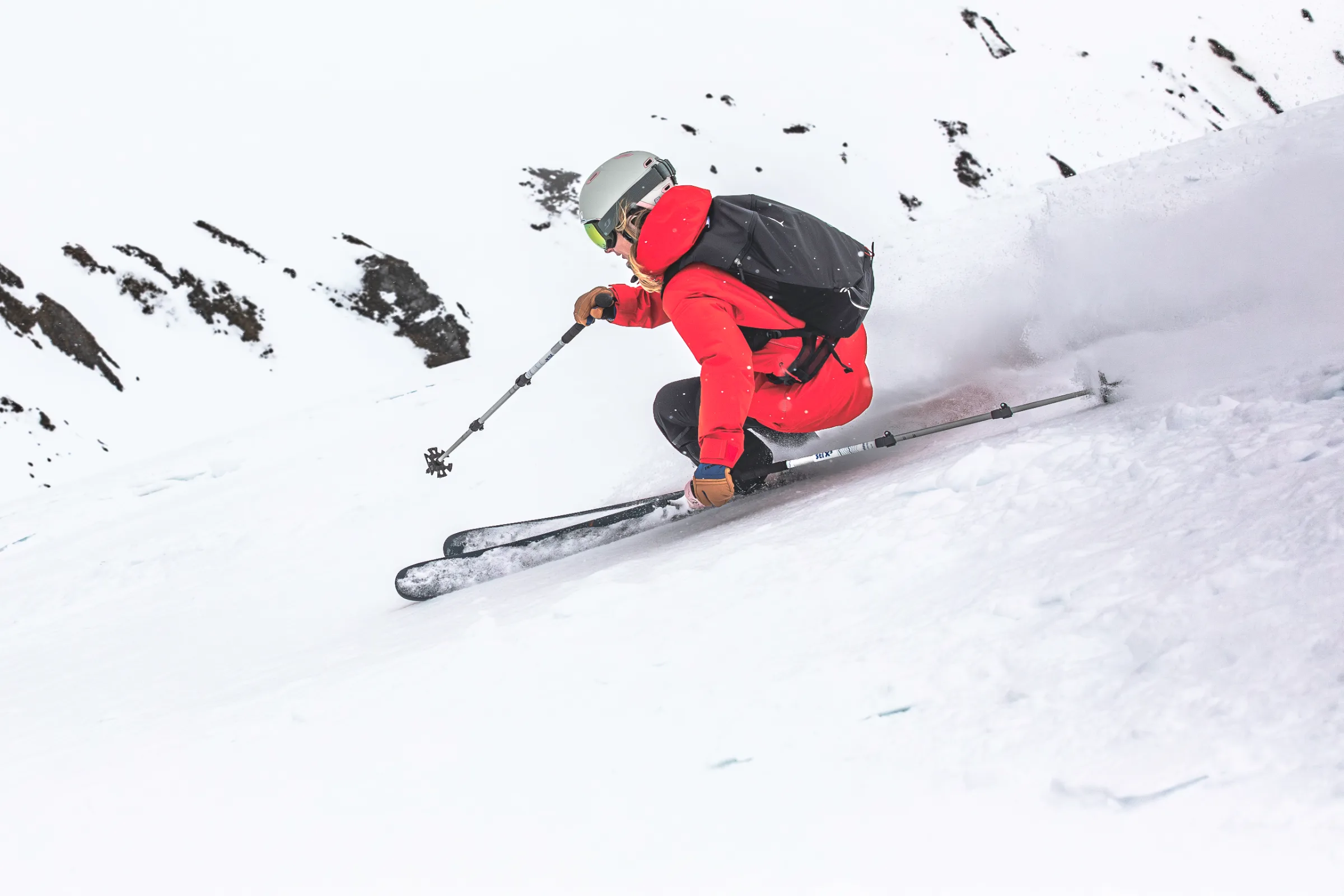 Von schräg hinten gesehen fährt Pia Vogt tief in die Knie gebeugt über einen steilen Schneehang und zieht eine Schneefahne hinter sich her.