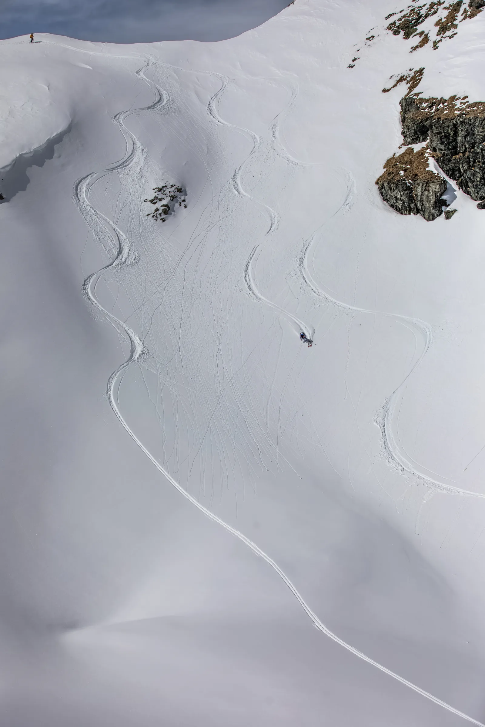 Pia Vogt zieht einen Schwung durch den Schnee unterhalb einer Felswand; lange S-förmige Skispuren durchziehen den weiten Hang in Lenzerheide.