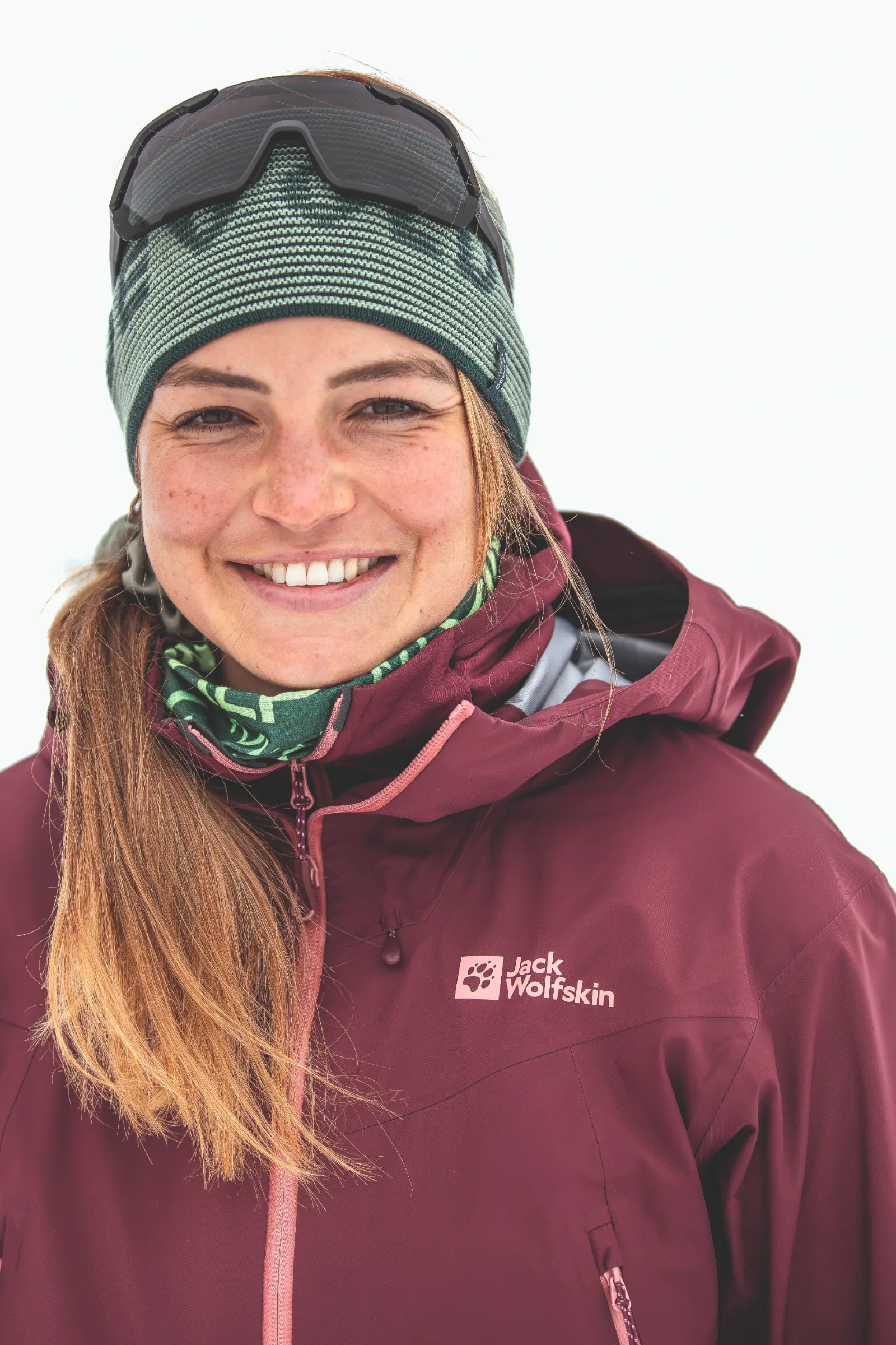 Ramona Arendt lächelt vor weißem Hintergrund in die Kamera, mit grünem Stirnband, hochgeschobener Sonnenbrille und burgunderroter Jacke.