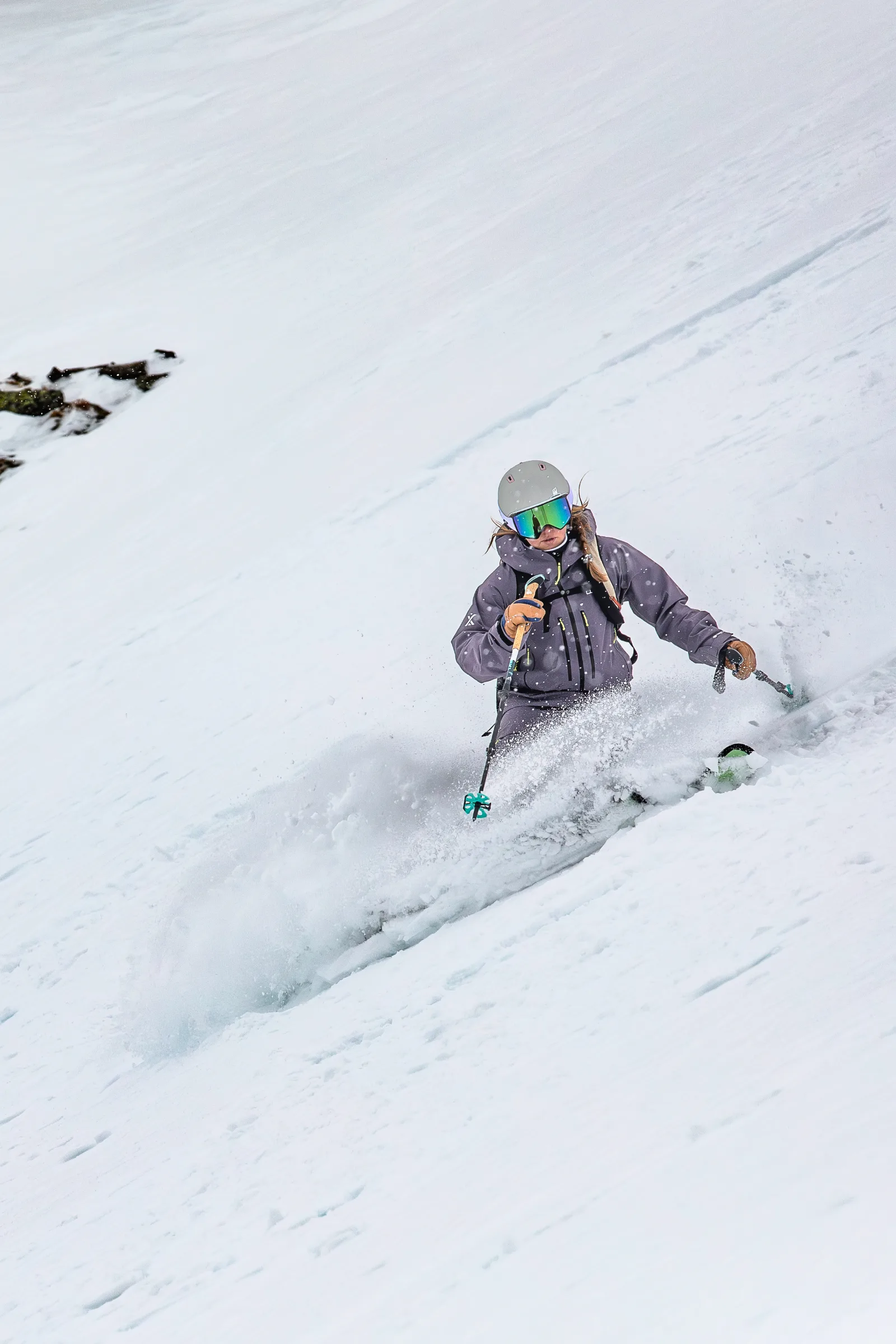 Ramona Arendt zieht mit Helm und verspiegelter Skibrille einen Schwung durch einen verschneiten Hang, wobei Schnee vor ihren Knien aufwirbelt.