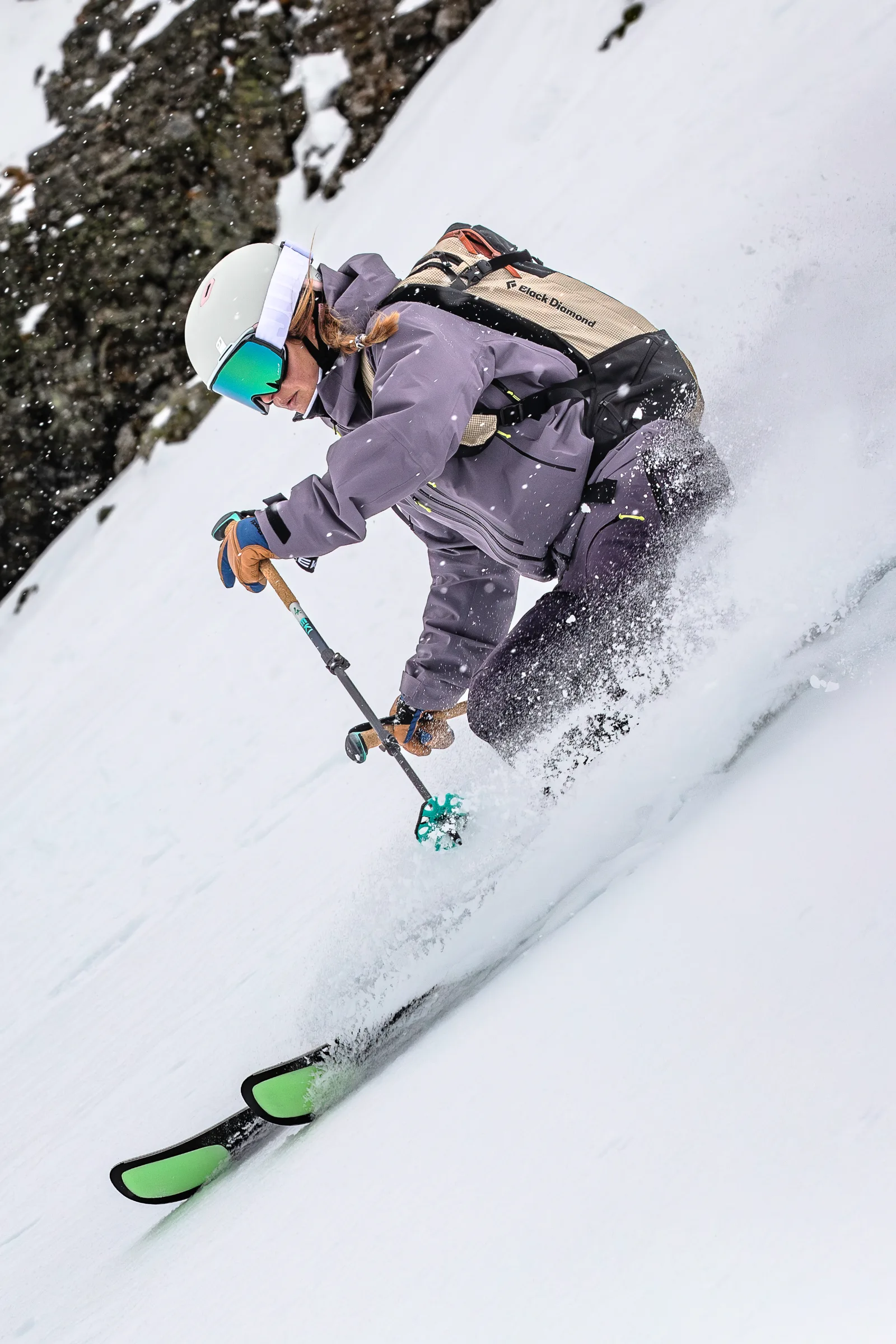Ramona Arendt lehnt sich neben einer Felswand tief in einen Skischwung, mit grün-schwarzen Skispitzen und aufspritzendem Schnee im Vordergrund.