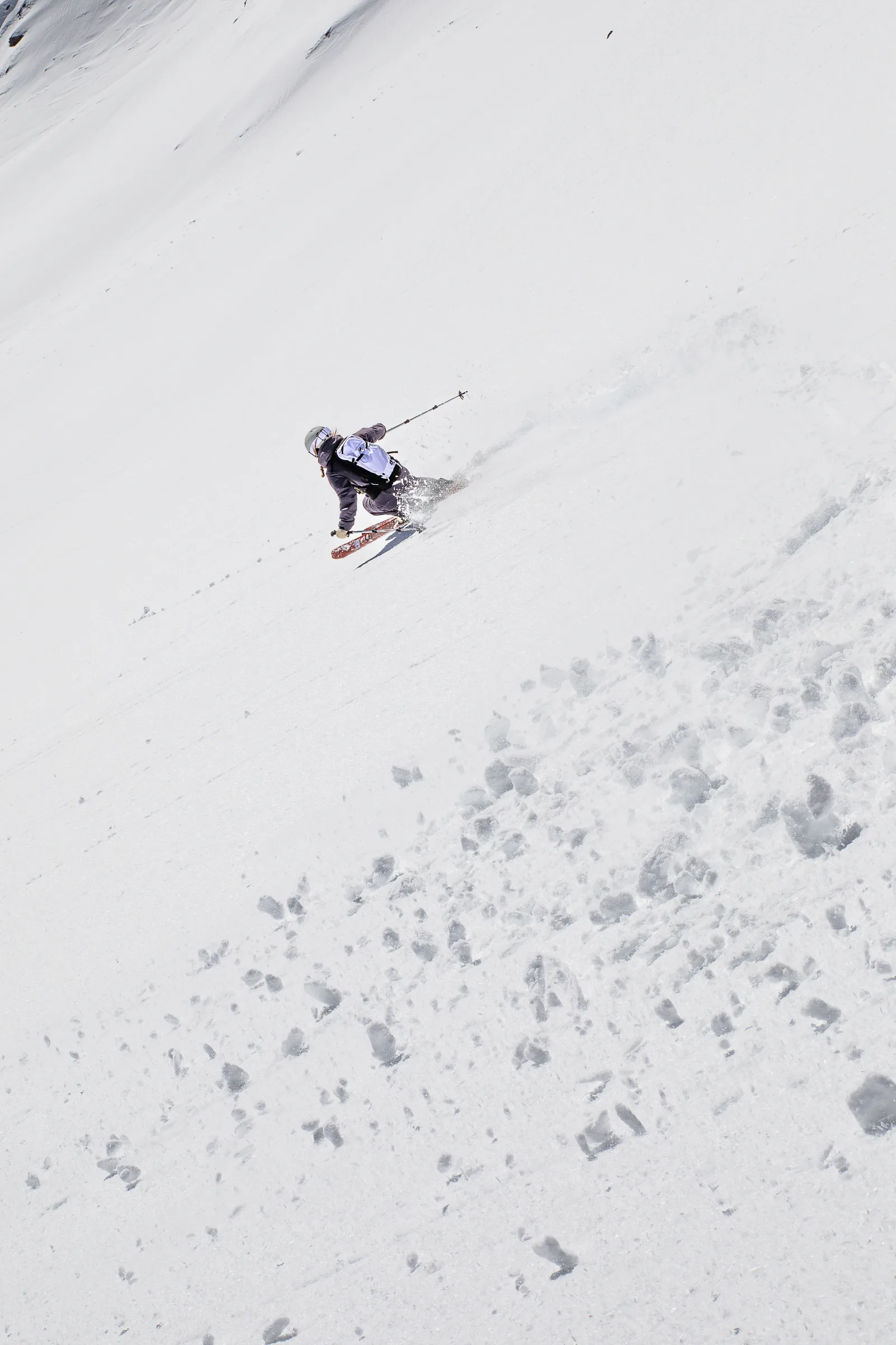 Von hinten gesehen fährt Ramona Arendt mit hellem Rucksack in tiefer Haltung einen weiten Schneehang hinab und wirbelt beim Schwung Schnee auf.