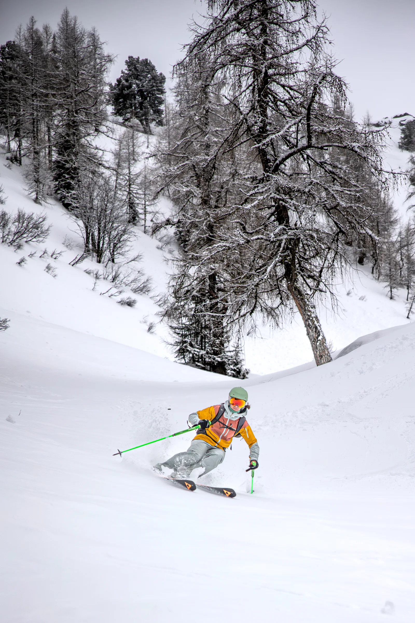 Sabine Speidel fährt mit grünen Skistöcken durch tiefen Schnee zwischen schneebedeckten Bäumen in Gastein.