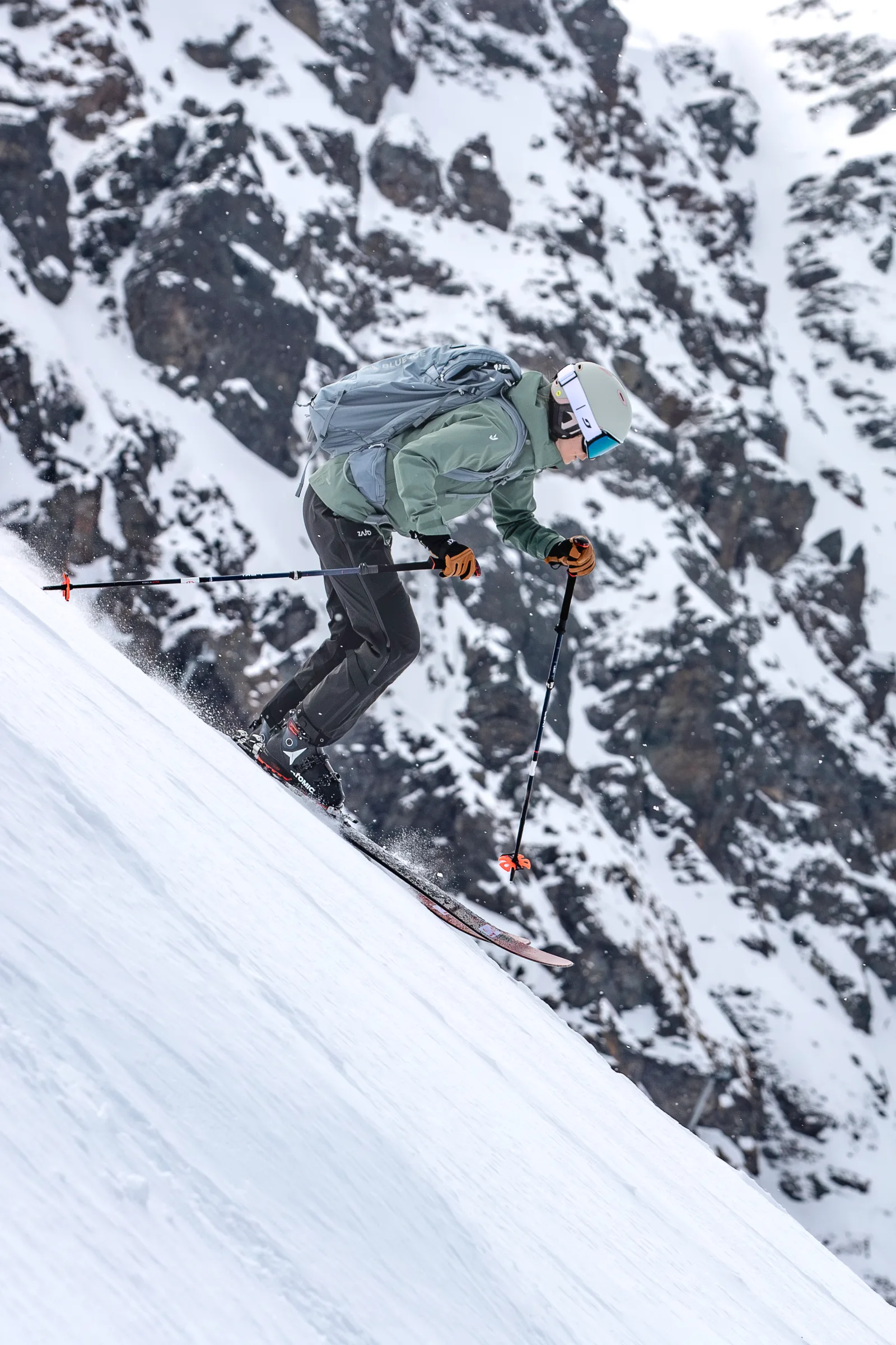 Sabrina Stickl fährt in grüner Jacke mit grauem Rucksack einen steilen Schneehang vor schneebedeckten Felswänden hinab.