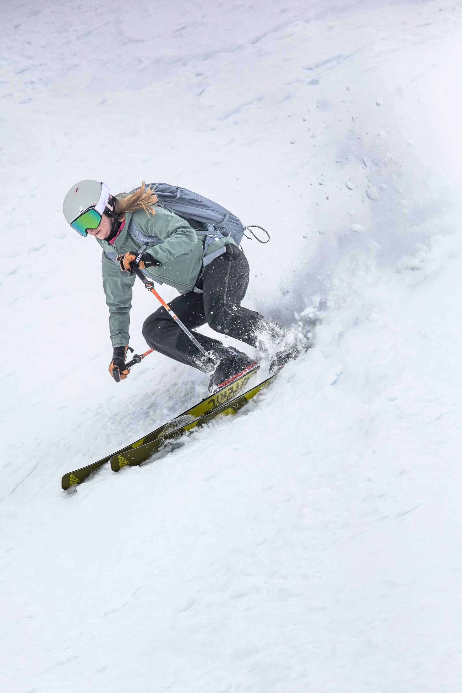 Sabrina Stickl kantet ihre Ski in einem engen Schwung auf und wirbelt Schnee auf; ihr Pferdeschwanz ragt unter dem Helm hervor.