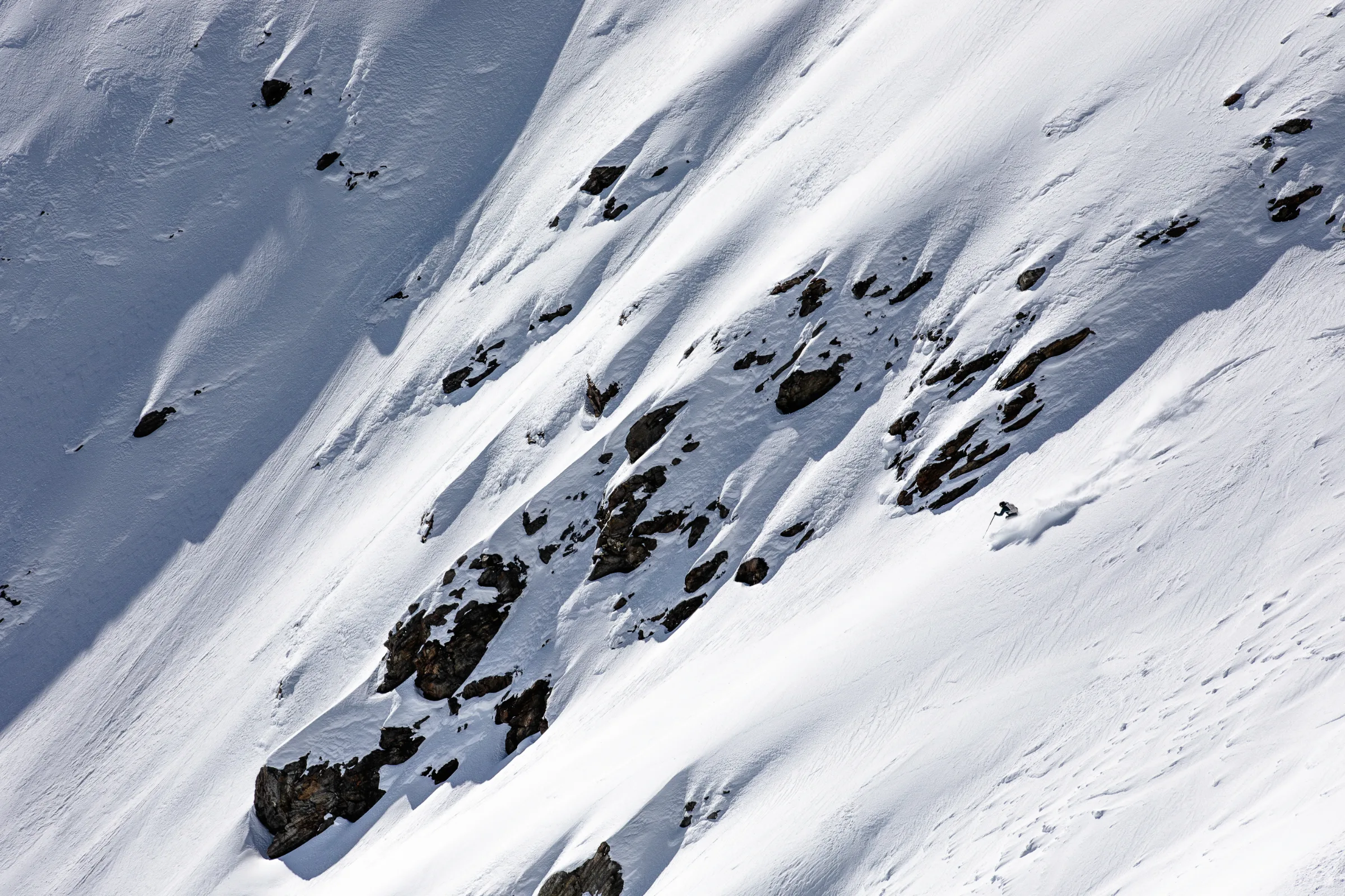 Simon Stickl zieht auf einem steilen, felsdurchsetzten Schneehang in Lenzerheide einen Schwung und wirbelt eine Schneewolke auf.